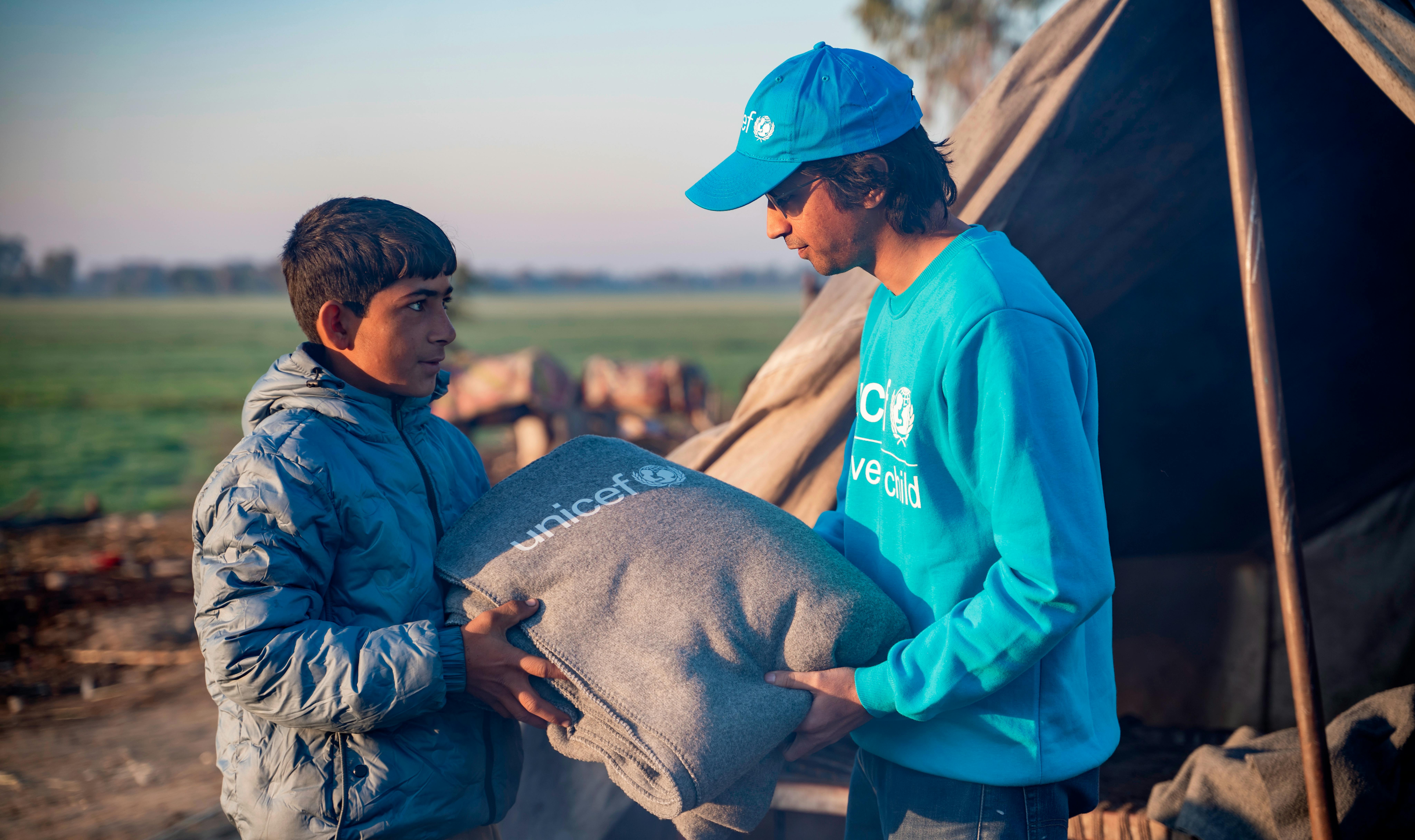 L'operatore UNICEF Moeed Hussain consegna una coperta al quattordicenne Munawwar durante la distribuzione dei kit invernali dell'UNICEF nel villaggio di Zangi Brohi, distretto di Dadu, Sindh.