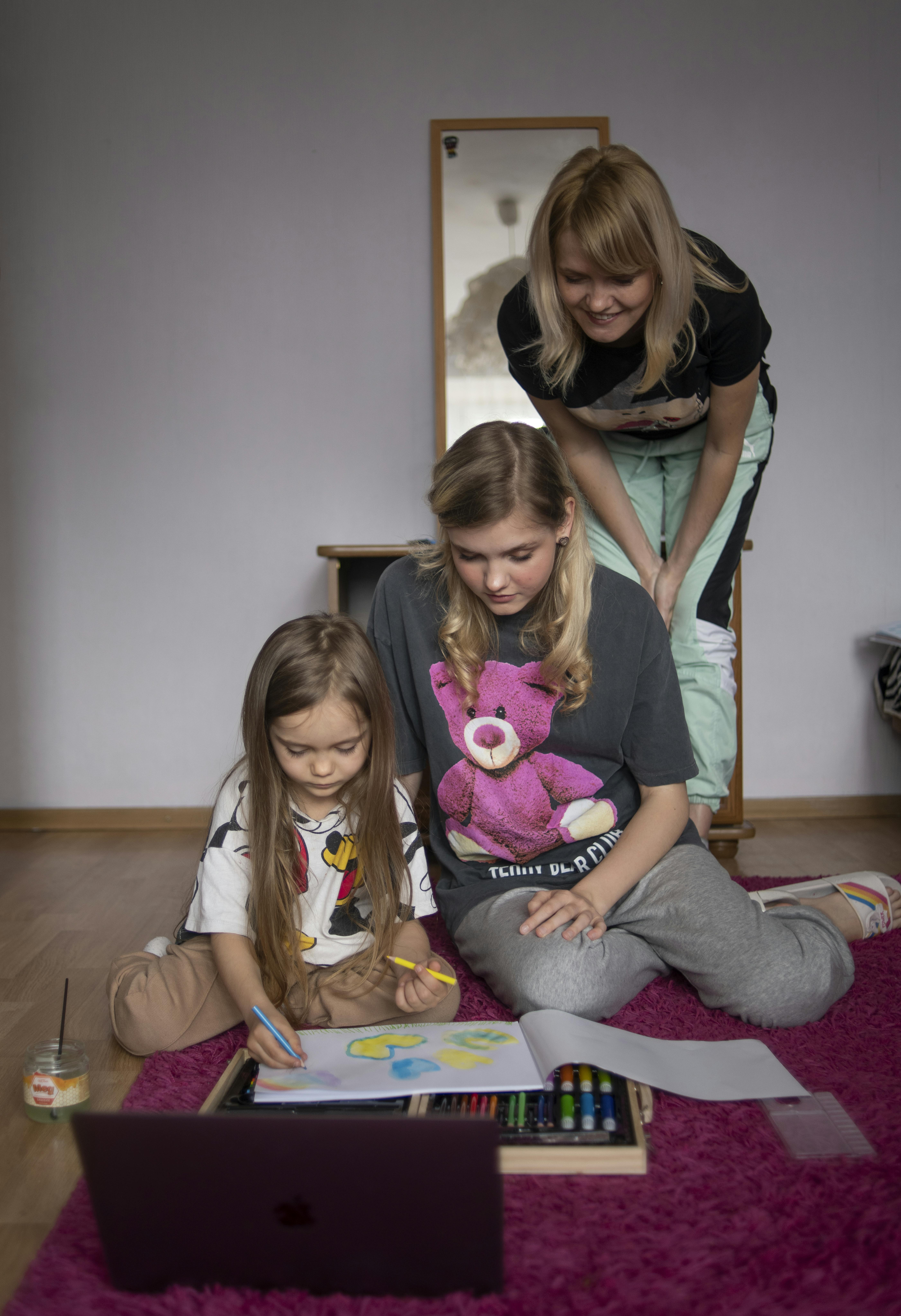 Oleksandra (al centro) e sua madre Anna (a destra) guardano mentre la piccola Katya disegna nel loro nuovo appartamento (temporaneo) a Varsavia, in Polonia.