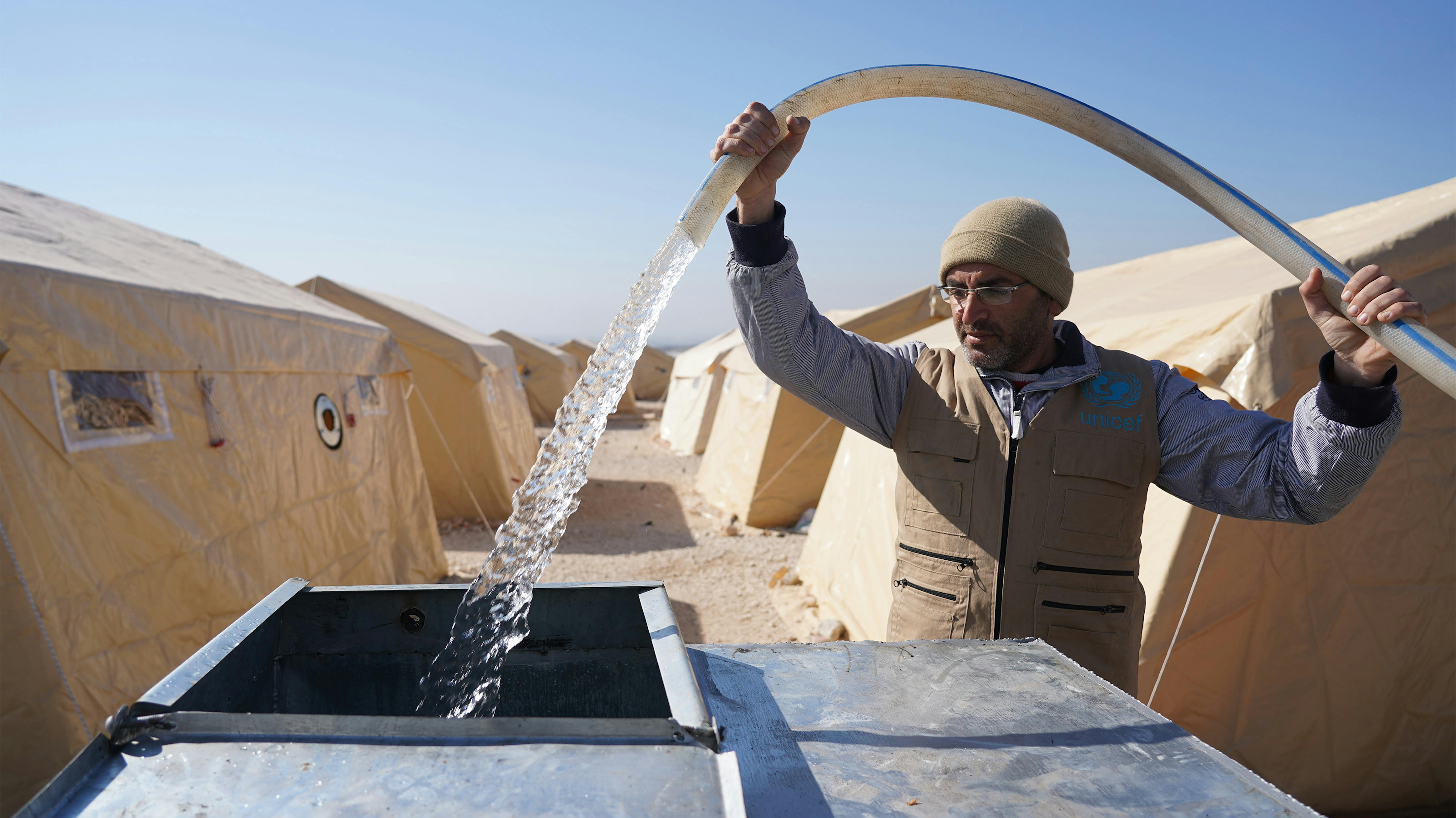 Siria - Staff partner dell'UNICEF Ihsan riempie i serbatoi d'acqua con acqua potabile per le famiglie sfollate che vivono nel campo di Al-Kamuna,