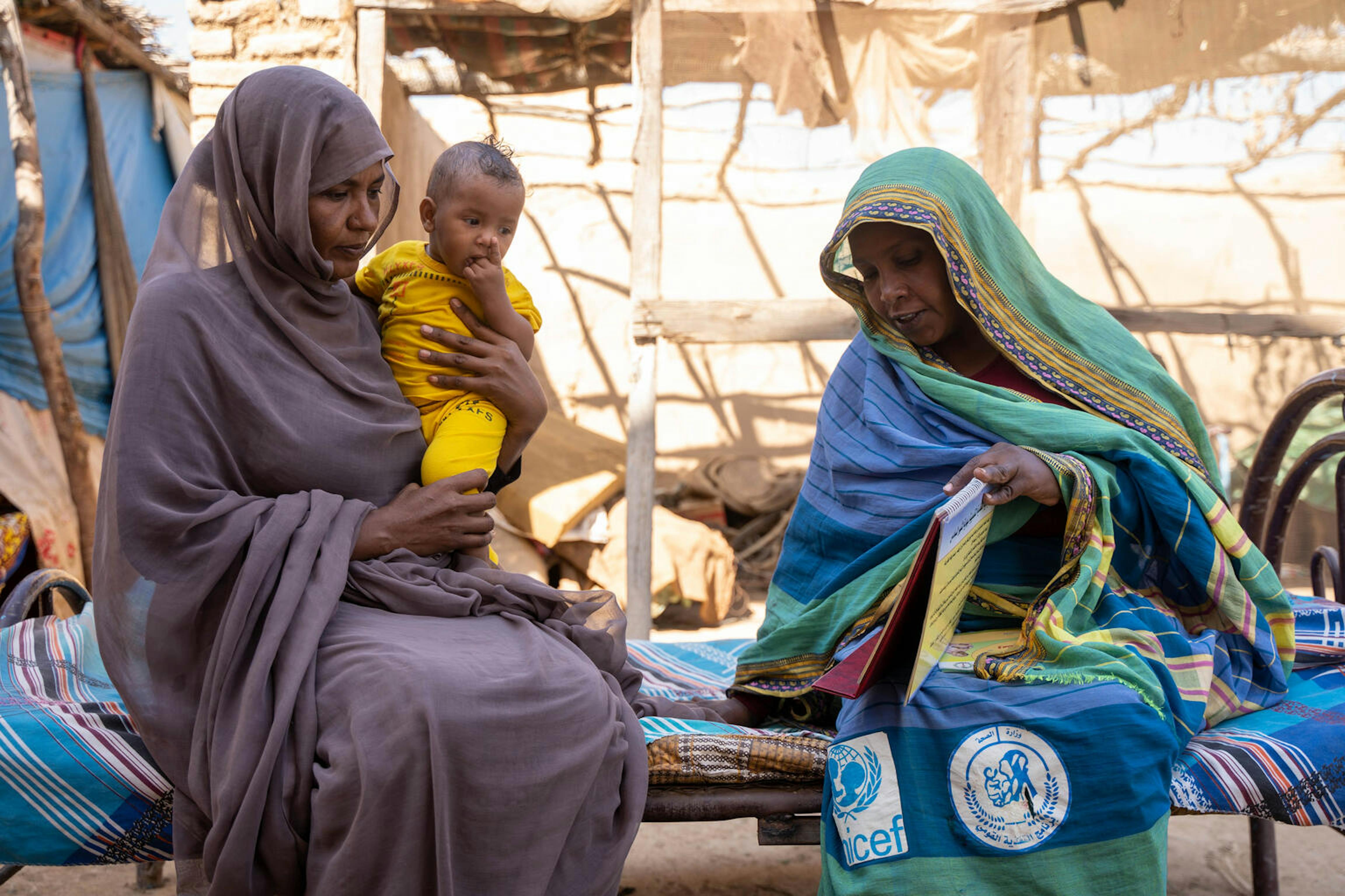 Sudan, Sabna Mohamed tiene la figlia di 9 mesi, Fatuma, in grembo mentre parla con una mamma del gruppo di supporto che la introduce al sostegno nutrizionale fornito dall'UNICEF