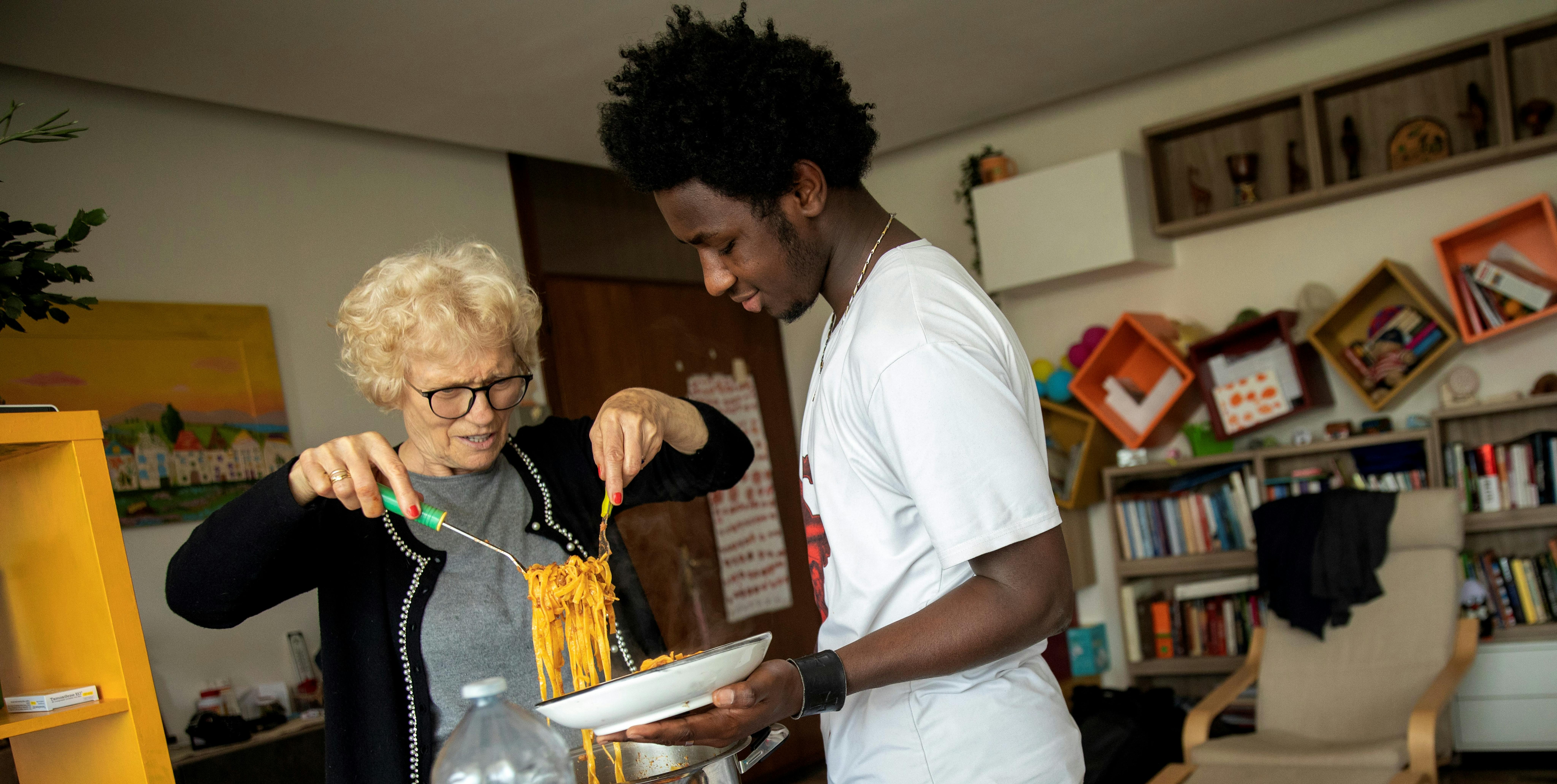 Mamajang e la sua nonna adottiva chiacchierano mentre servono tagliatelle al ragù per il pranzo di famiglia