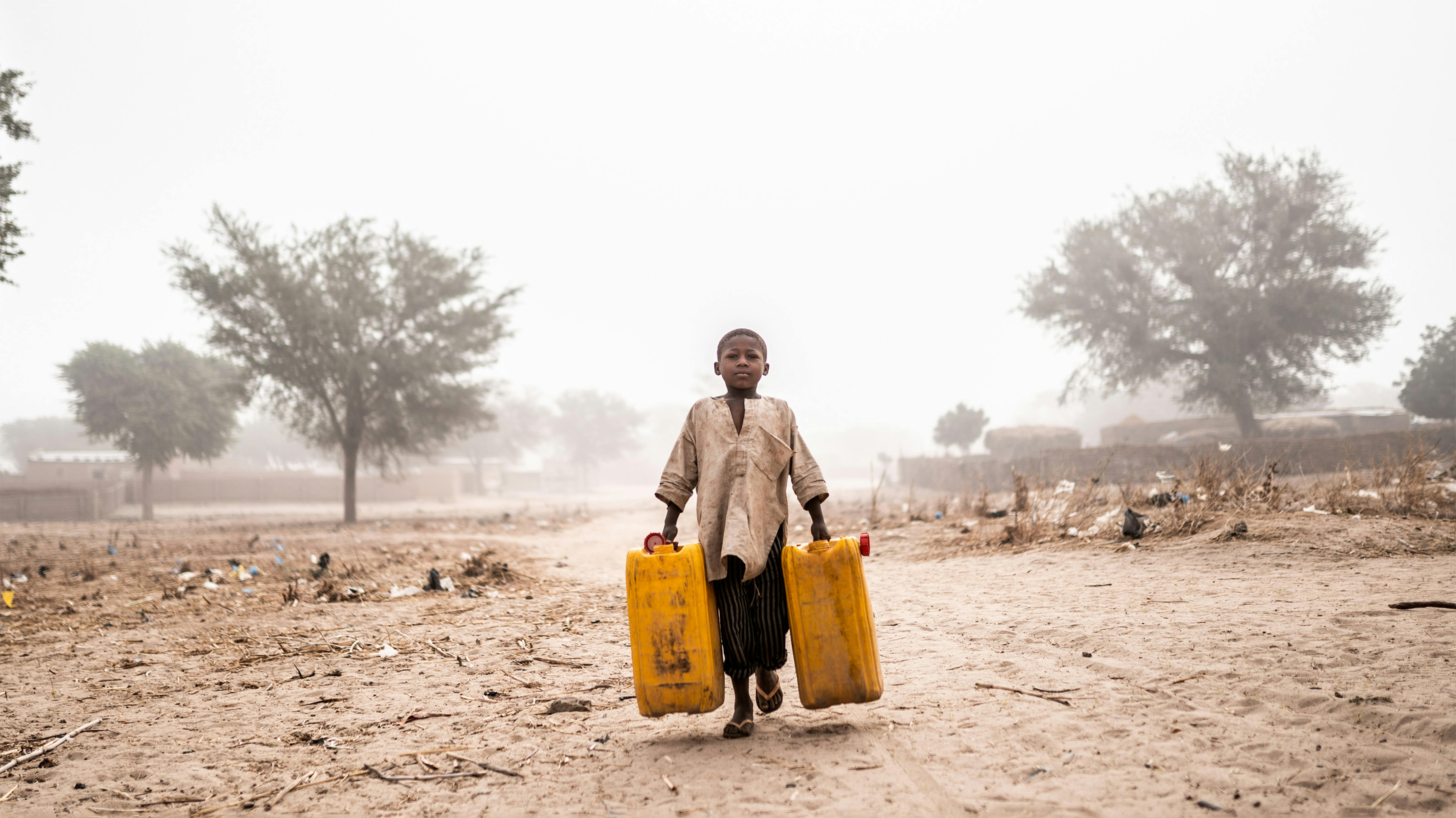 Nigeria -La mattina presto, coperto da polvere e vento, un bambino va a prendere l'acqua al punto d'acqua più vicino nel villaggio di Tchadi, a 15 chilometri di distanza vicino al confine con il Niger