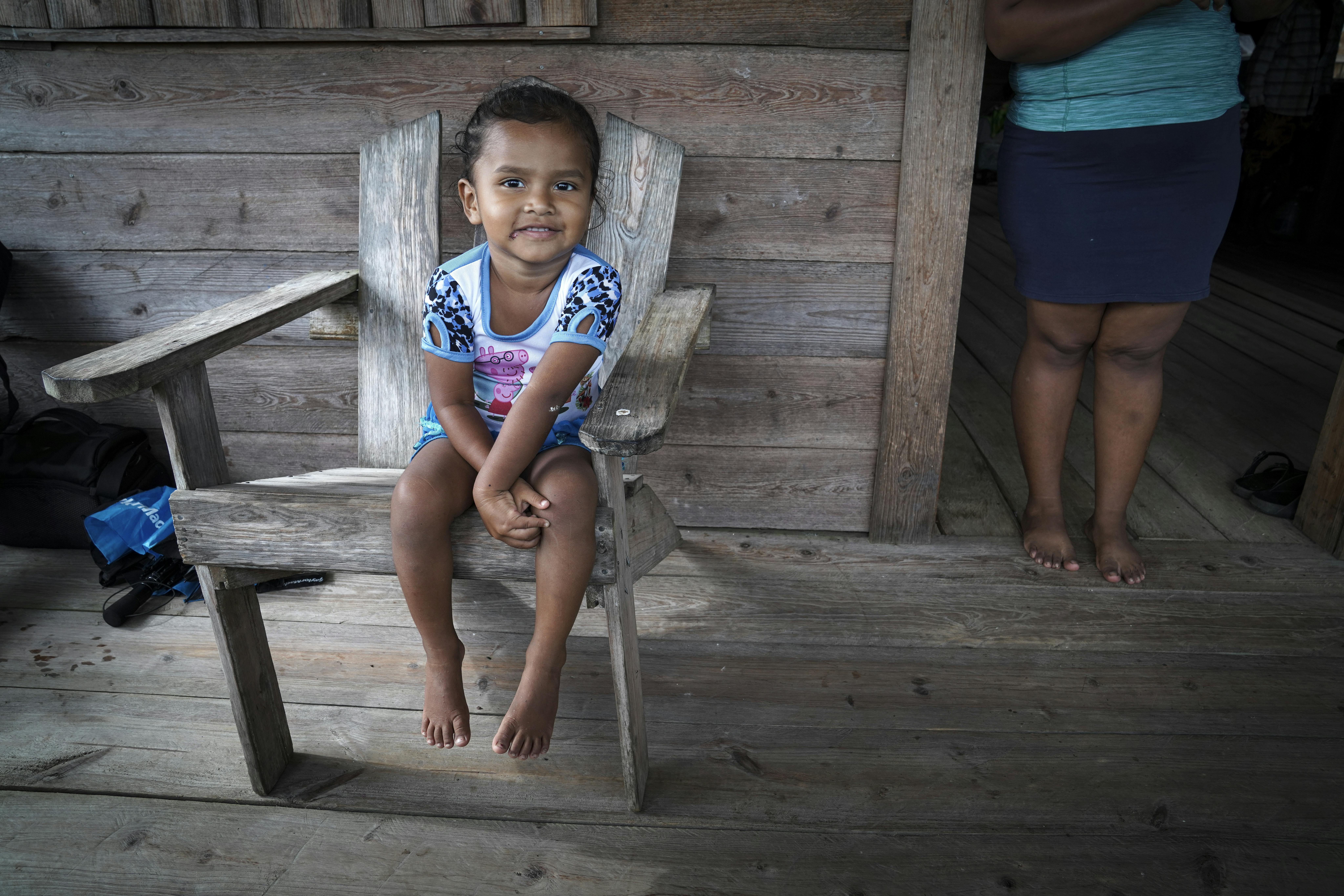 Rihanna, 3 anni, siede su una sedia di legno sotto il portico di casa mentre sua madre, Florencia, parla con il personale sanitario