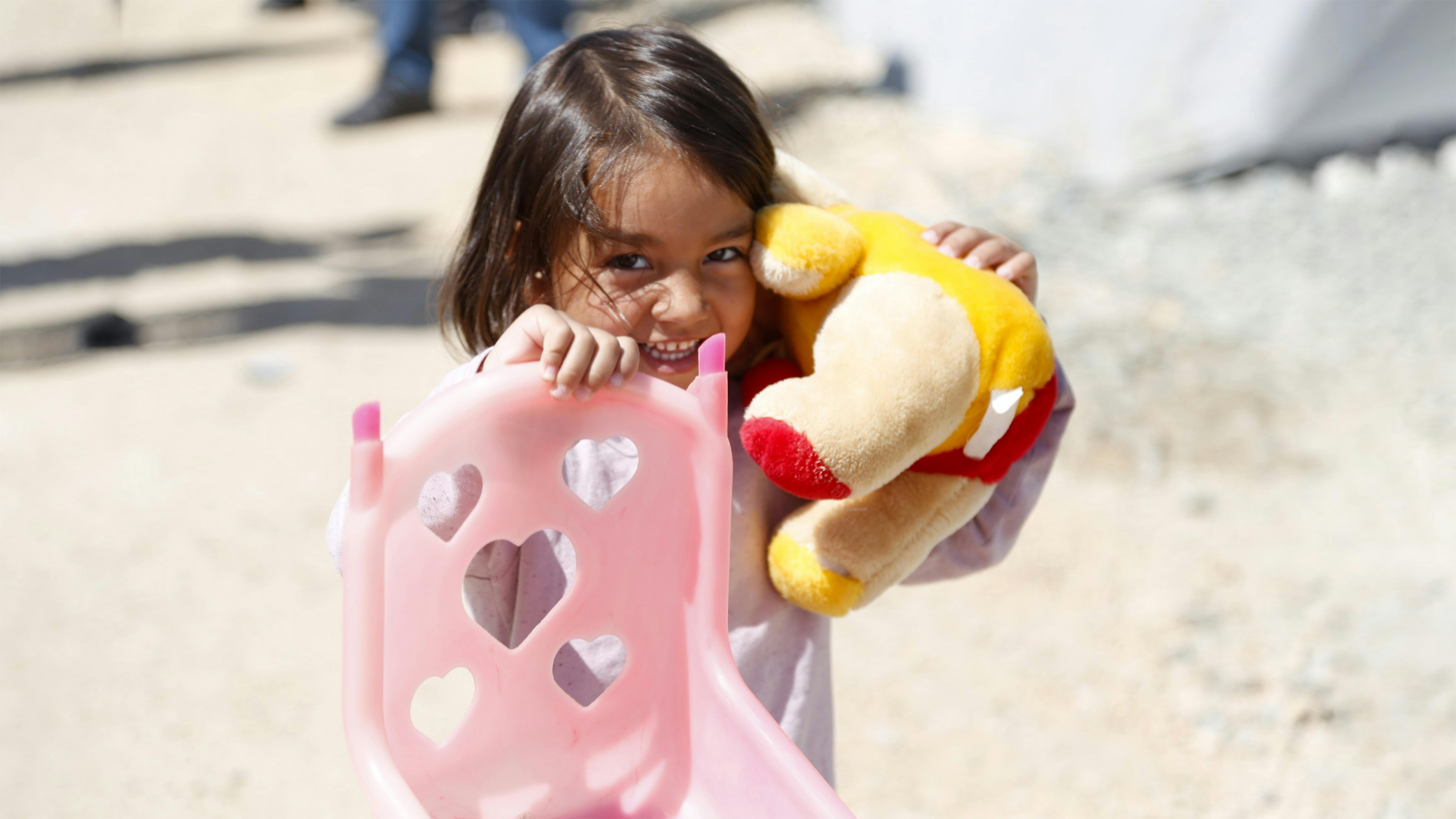 Una bambina che sorride e porta i suoi giocattoli nel rifugio temporaneo di Selam Camii a Hatay, dopo che due devastanti terremoti hanno colpito il sud-est della Turchia.