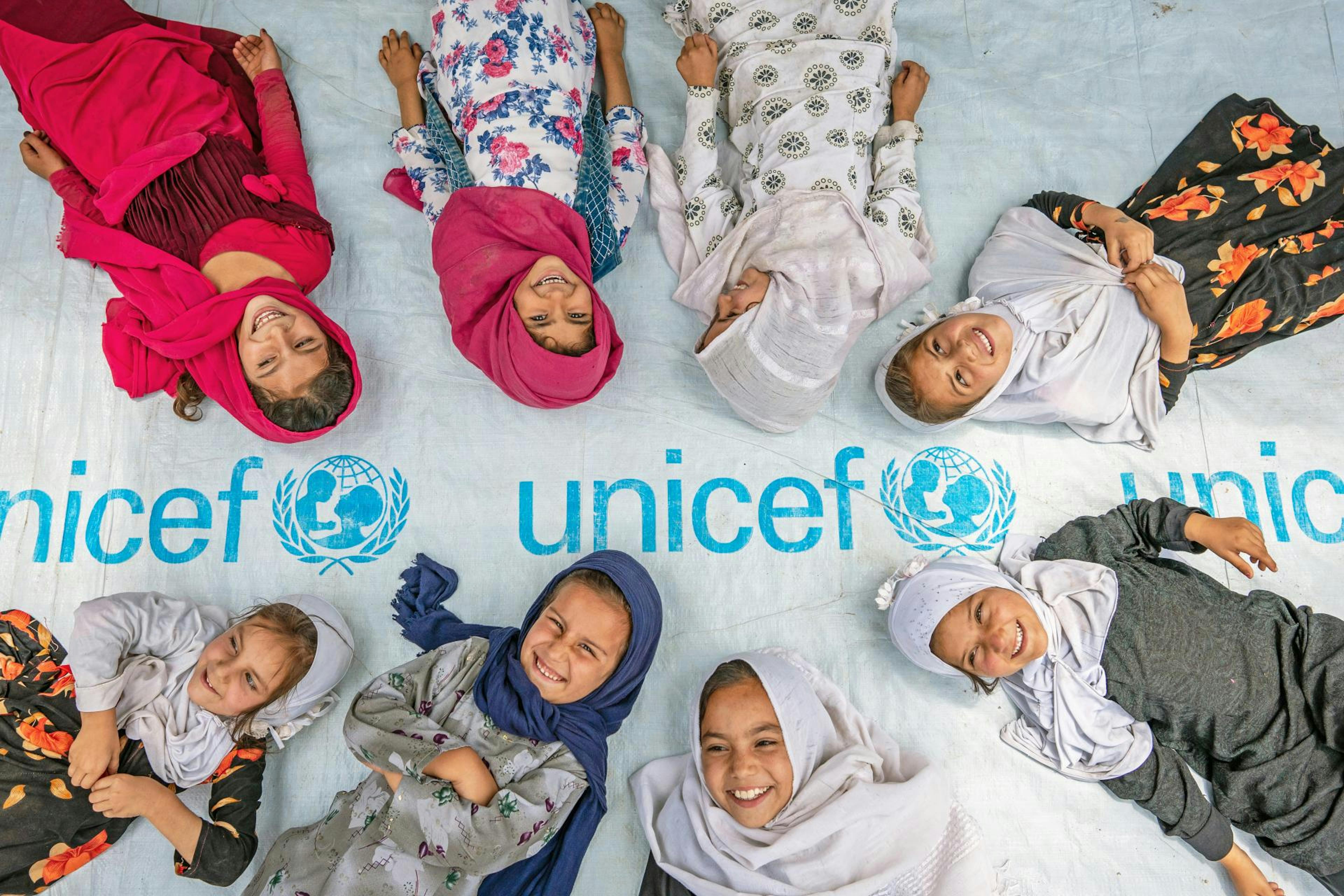 Bambine distese su un telo UNICEF, sorridono. Cover Annual Report