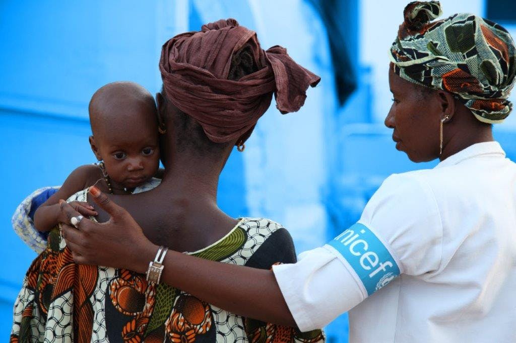 Bambina in braccio alla mamma tiene la mano di un'operatrice UNICEF