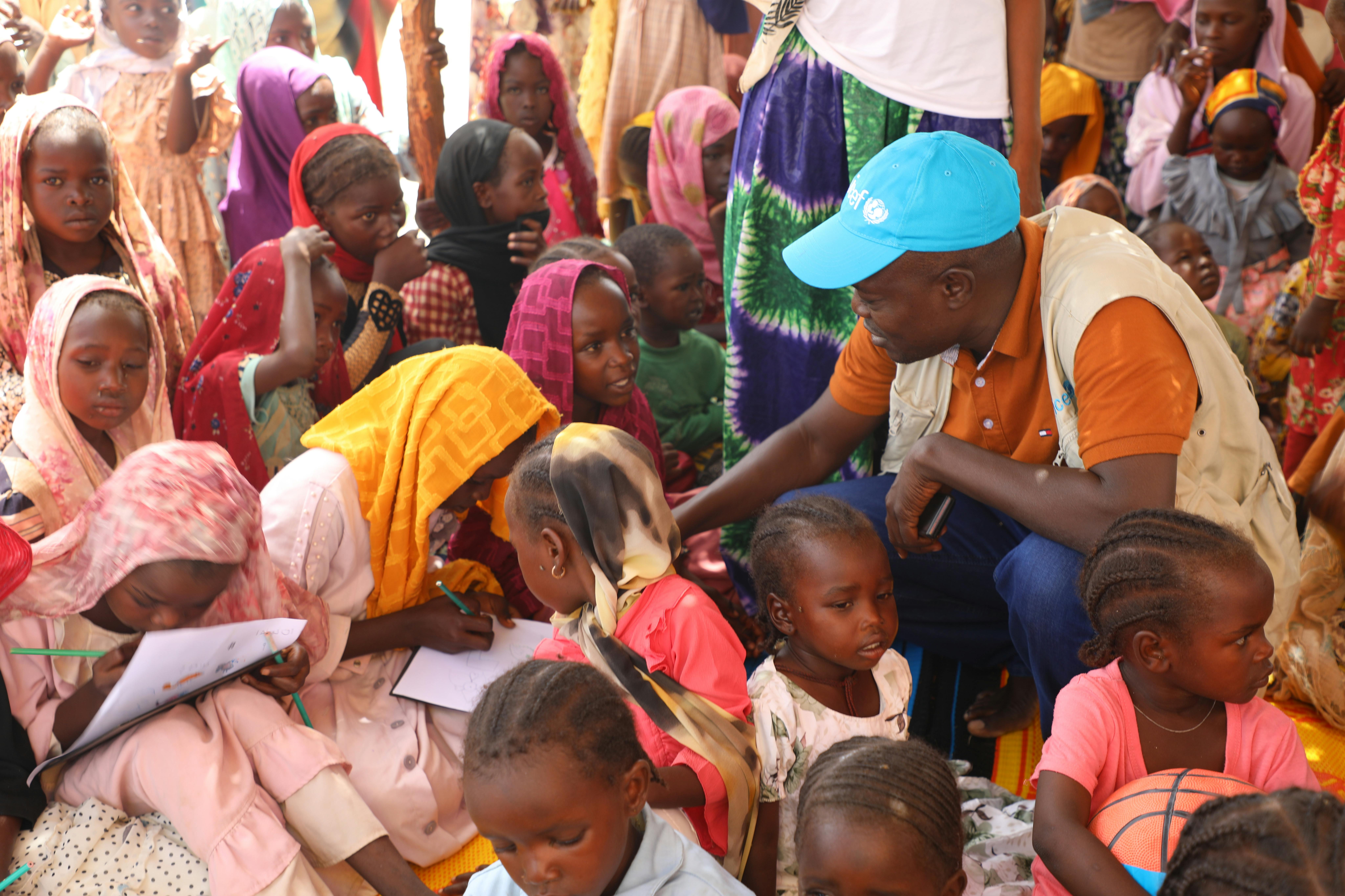 Valery Nodjimadji, specialista per la Protezione di UNICEF Ciad, è seduto con alcuni bambini nel Child-Friendly Space di Koufroun. Il centro è gestito dalla Croce Rossa Ciad, partner dell’UNICEF. Qui i bambini possono divertirsi, stare insieme ai loro pari e ricevere supporto psicosociale.
