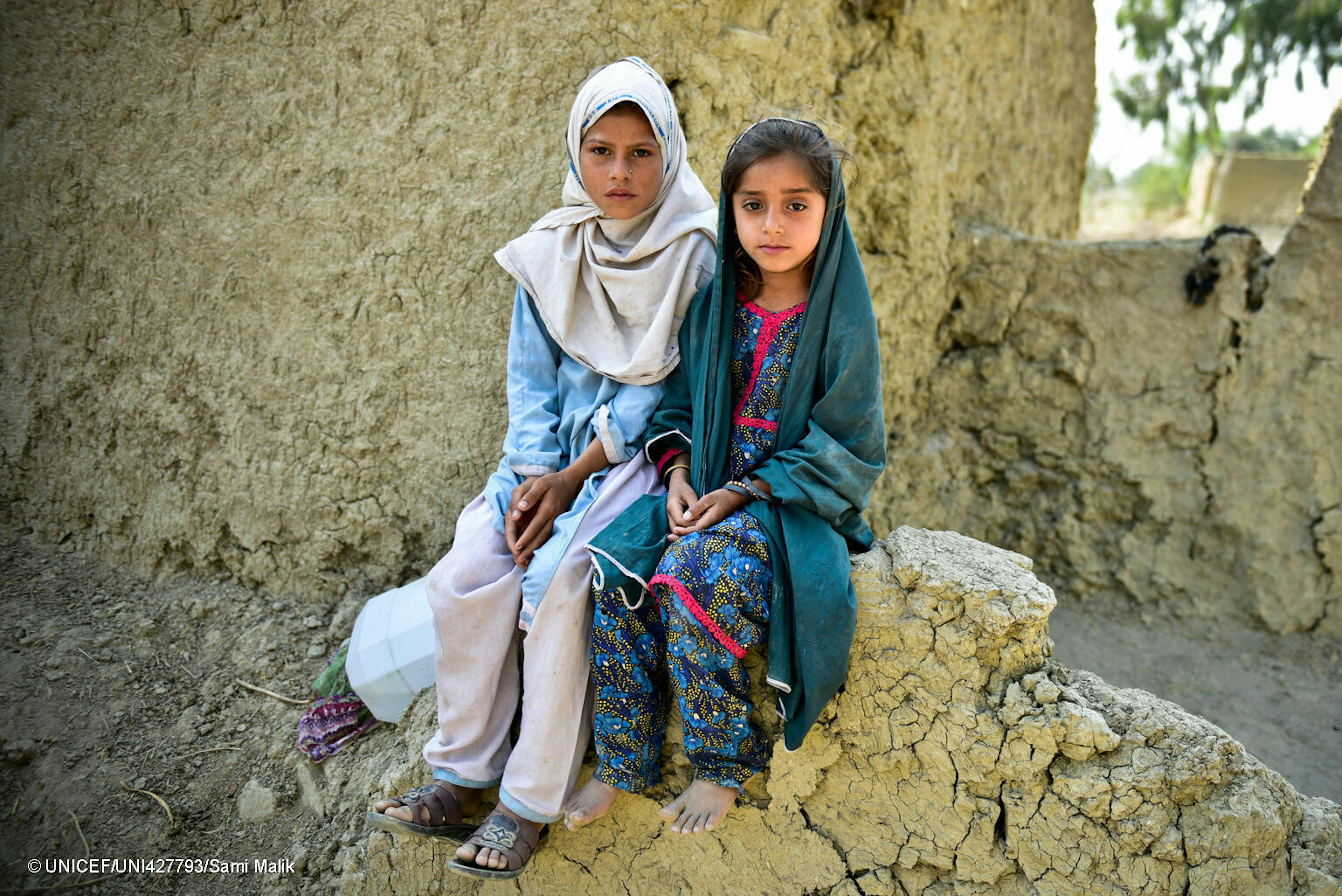 ©UNICEF/UNI427793/Sami Malik Muriko bibi (7) e Tehseen (6) siedono sul muro danneggiato della loro casa di fango che è stata quasi del tutto distrutta