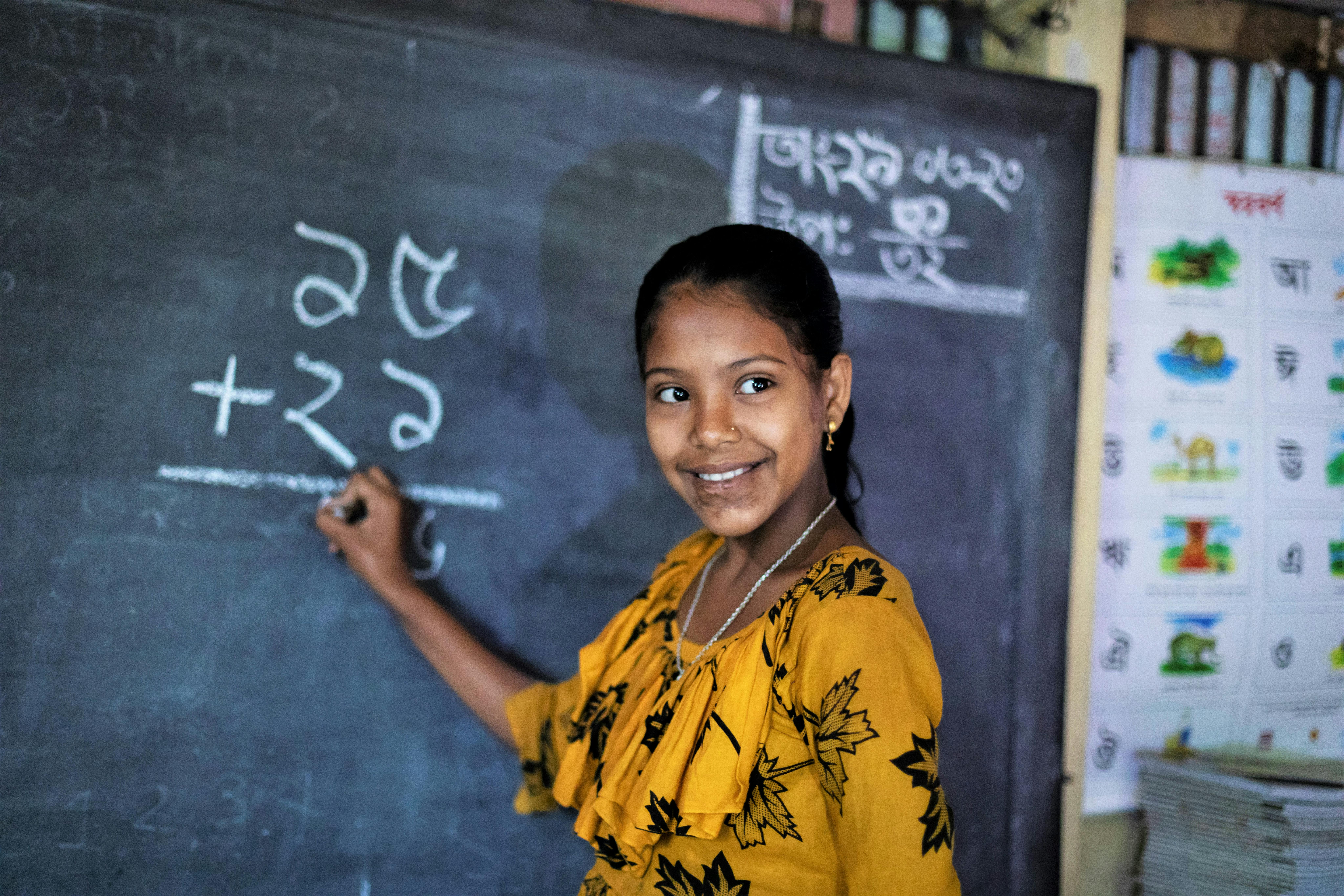 bambina del bangladesh scrive alla lavagna, sorride con il gesso in mano
