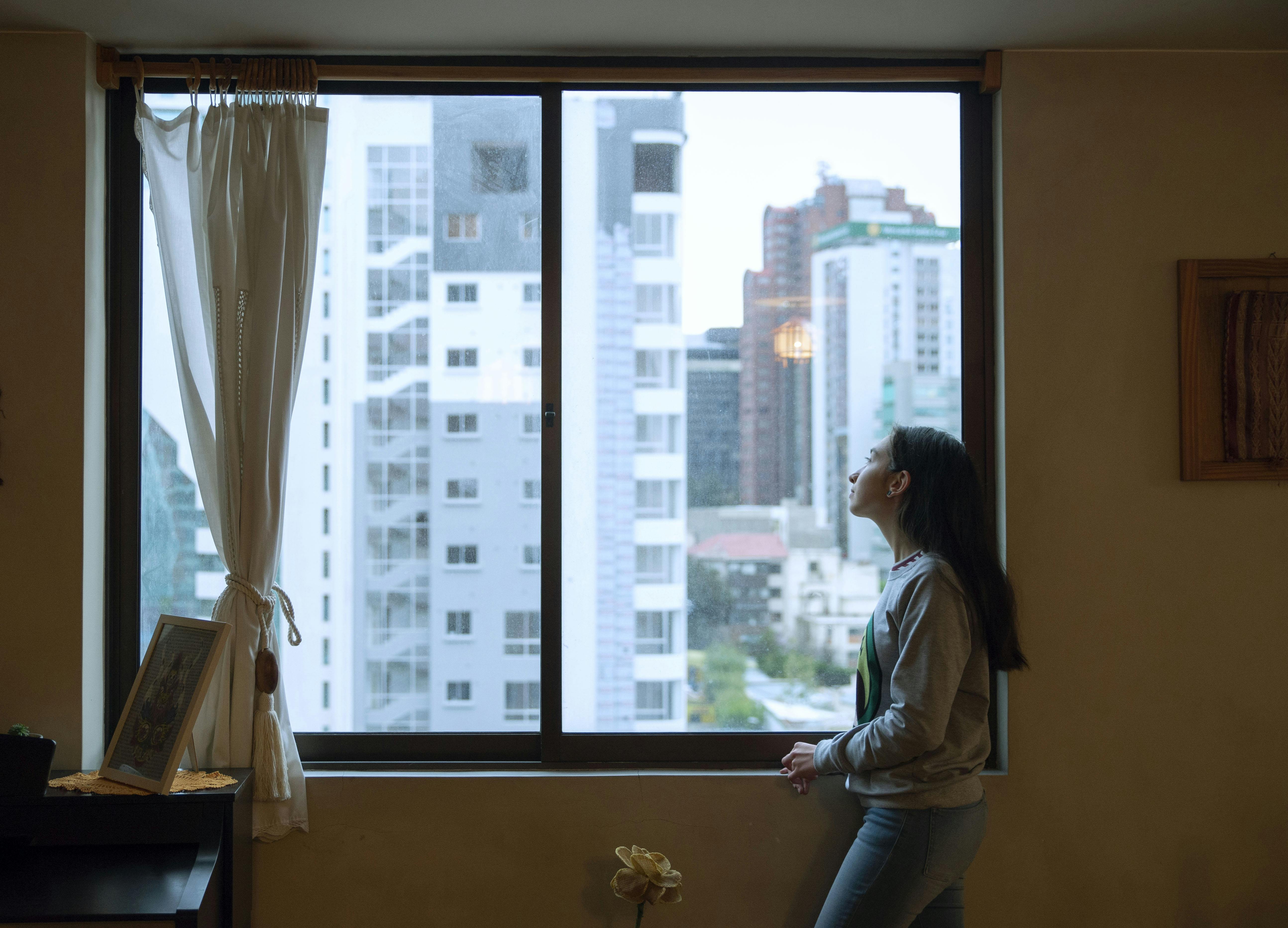 Ragazza guarda alla finestra, da un appartamento in città. Hero Salute Mentale