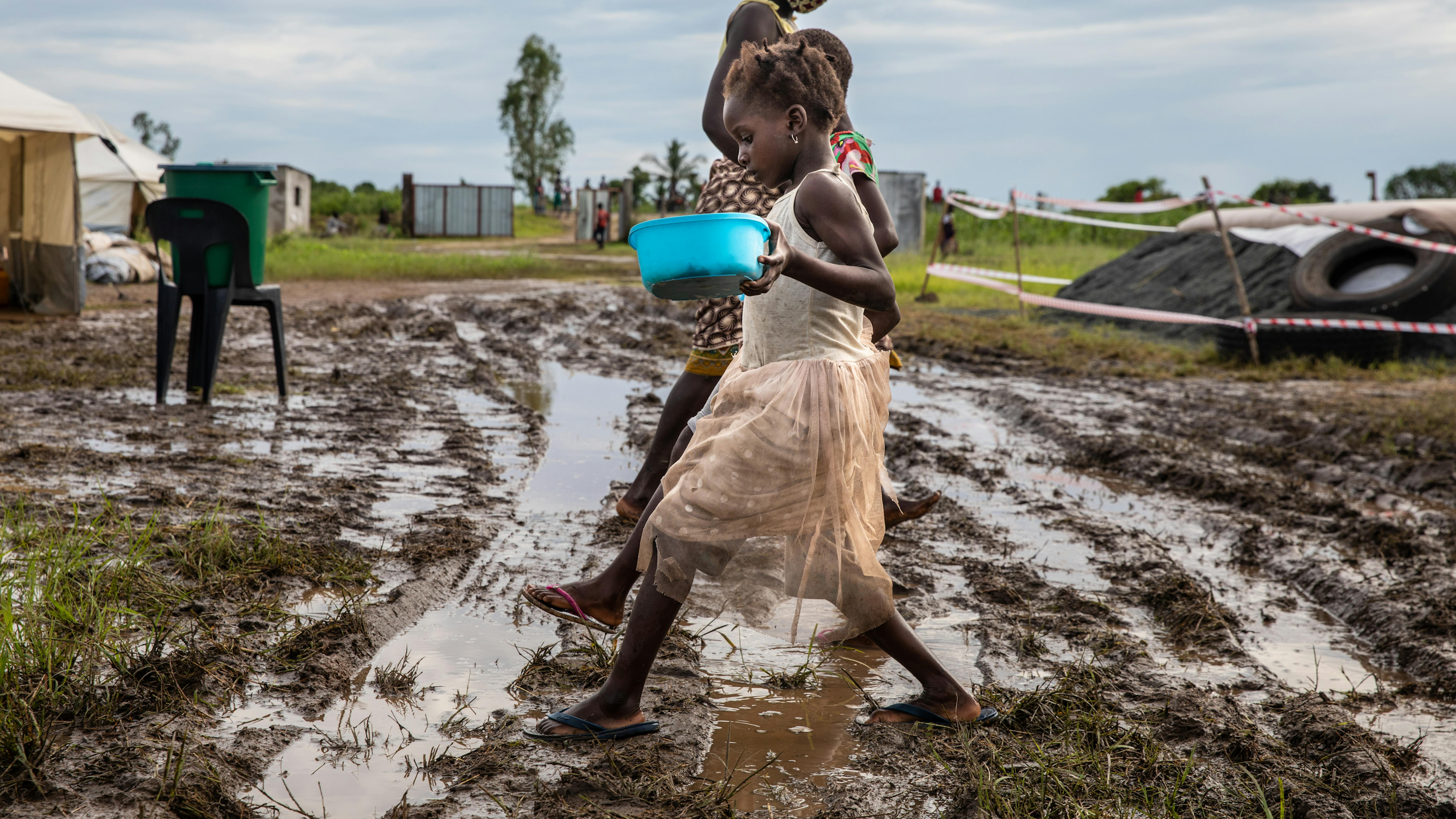 Mozambico, bambini camminano in una zona fangosa con contenitori di cibo ricevuti durante una distribuzione al Tica Relocation Center,