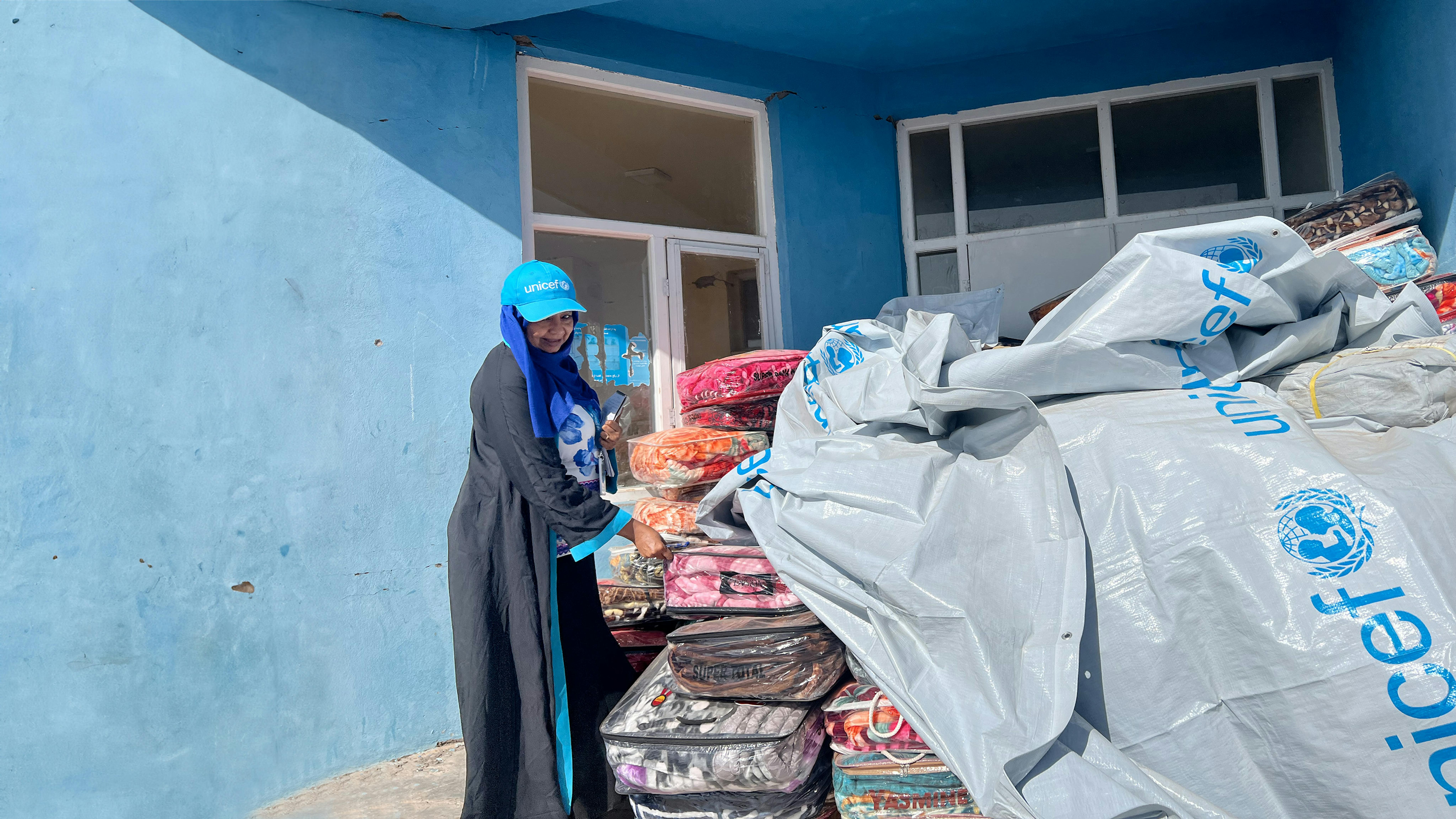 Tahani Elmobasher, specialista dell'UNICEF per la protezione dell'infanzia, accanto alle coperte e ai teloni distribuiti alle famiglie dall'UNICEF nel villaggio di Seyab