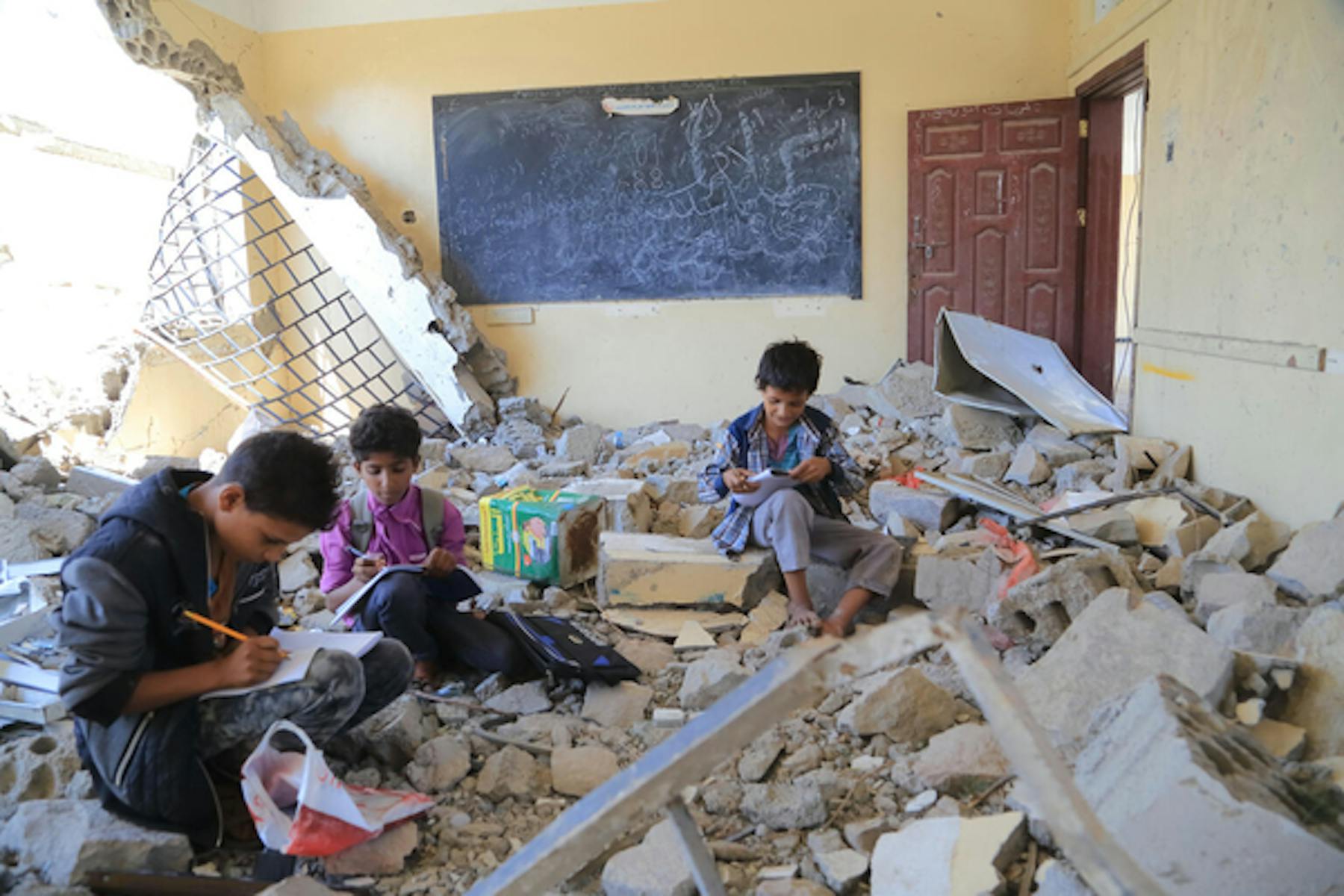 Alcuni bambini fanno i compiti tra le macerie della loro scuola a Taiz, in Yemen