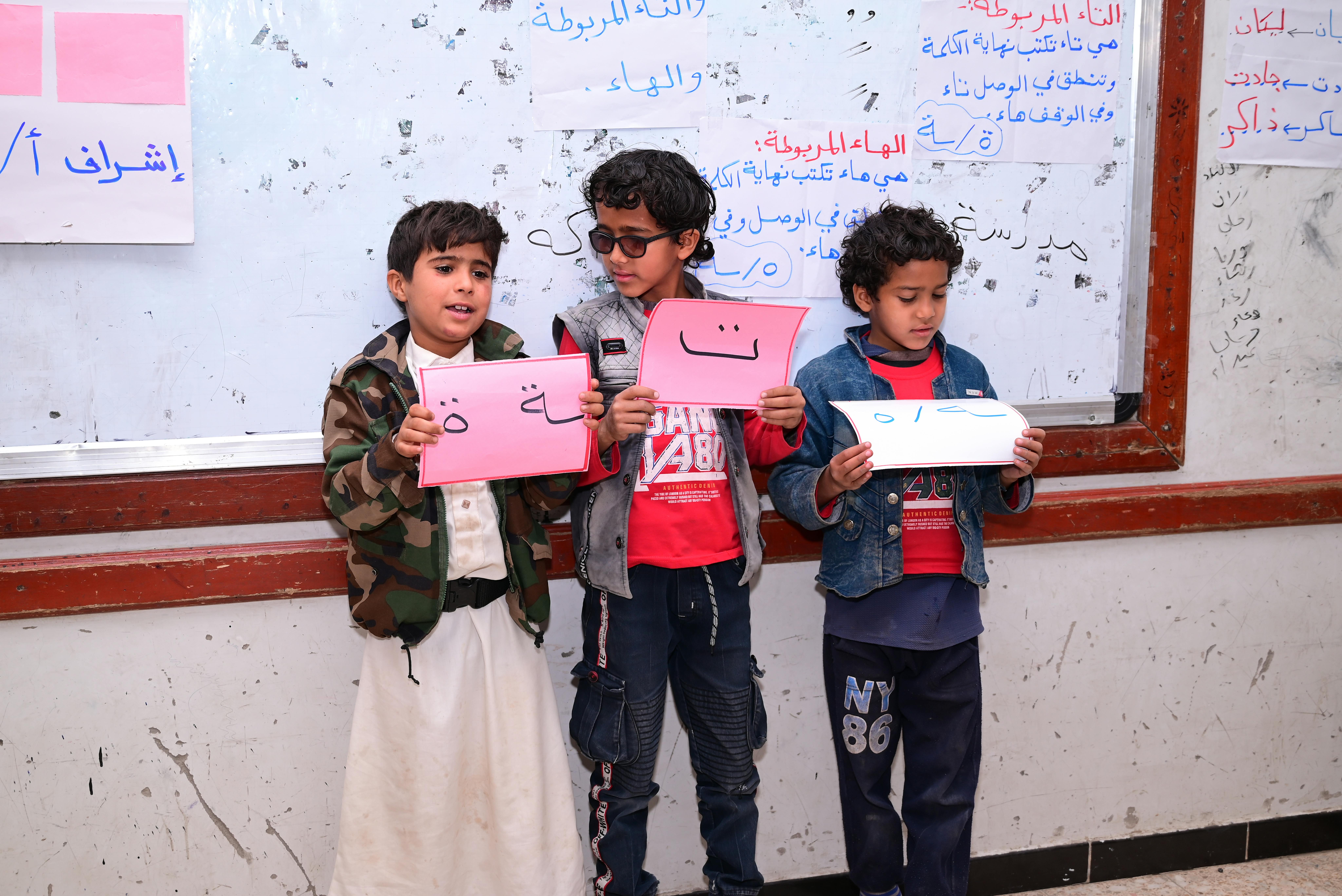 Rakan con due suoi compagni di classe tengono in mano alcuni ritagli di carta durante una delle attività di recupero presso la scuola Al Gardai a Sana'a, in Yemen.