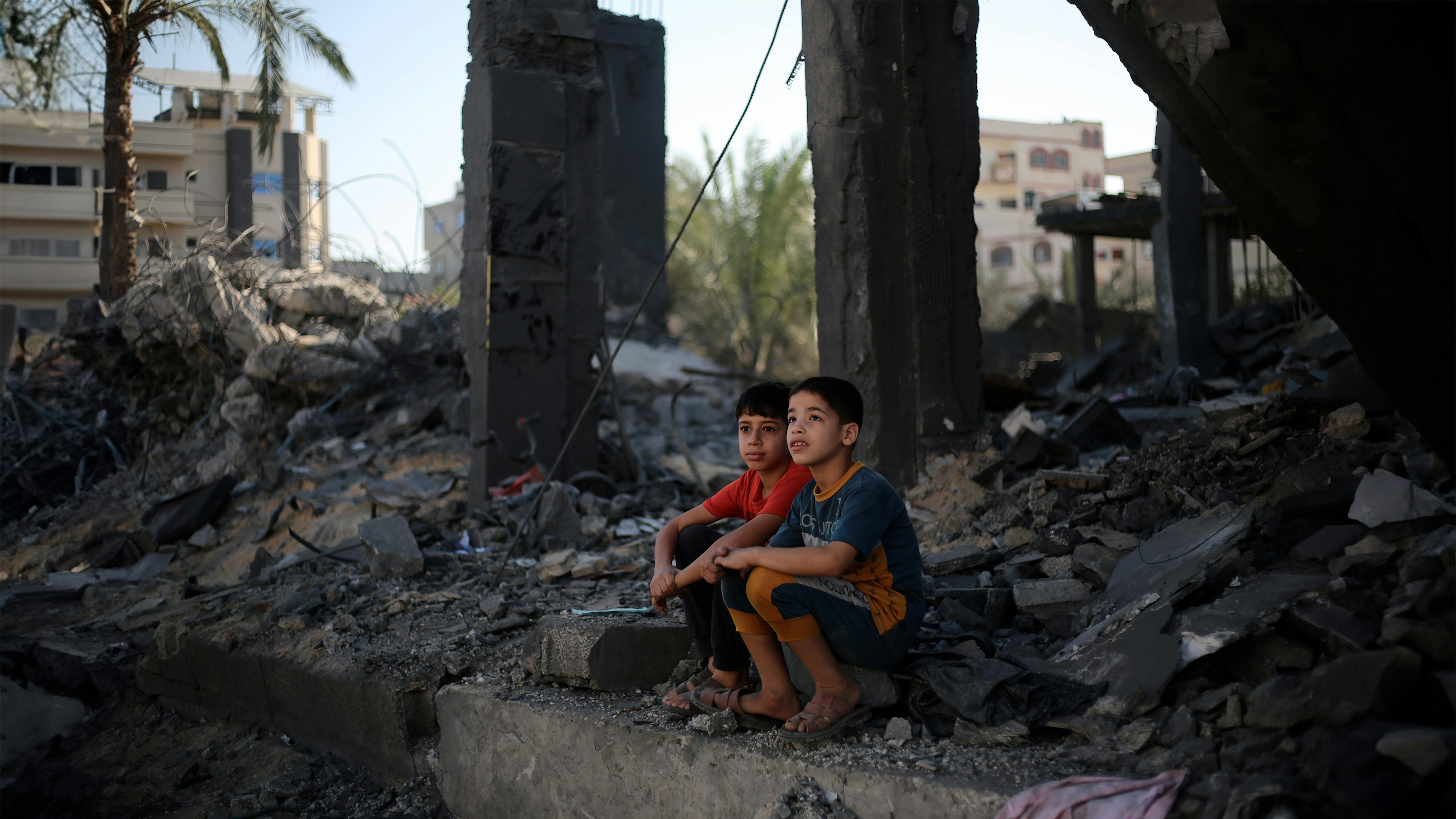 Due bambini palestinesi seduti tra le macerie di ciò che resta della loro casa nella città di Rafah