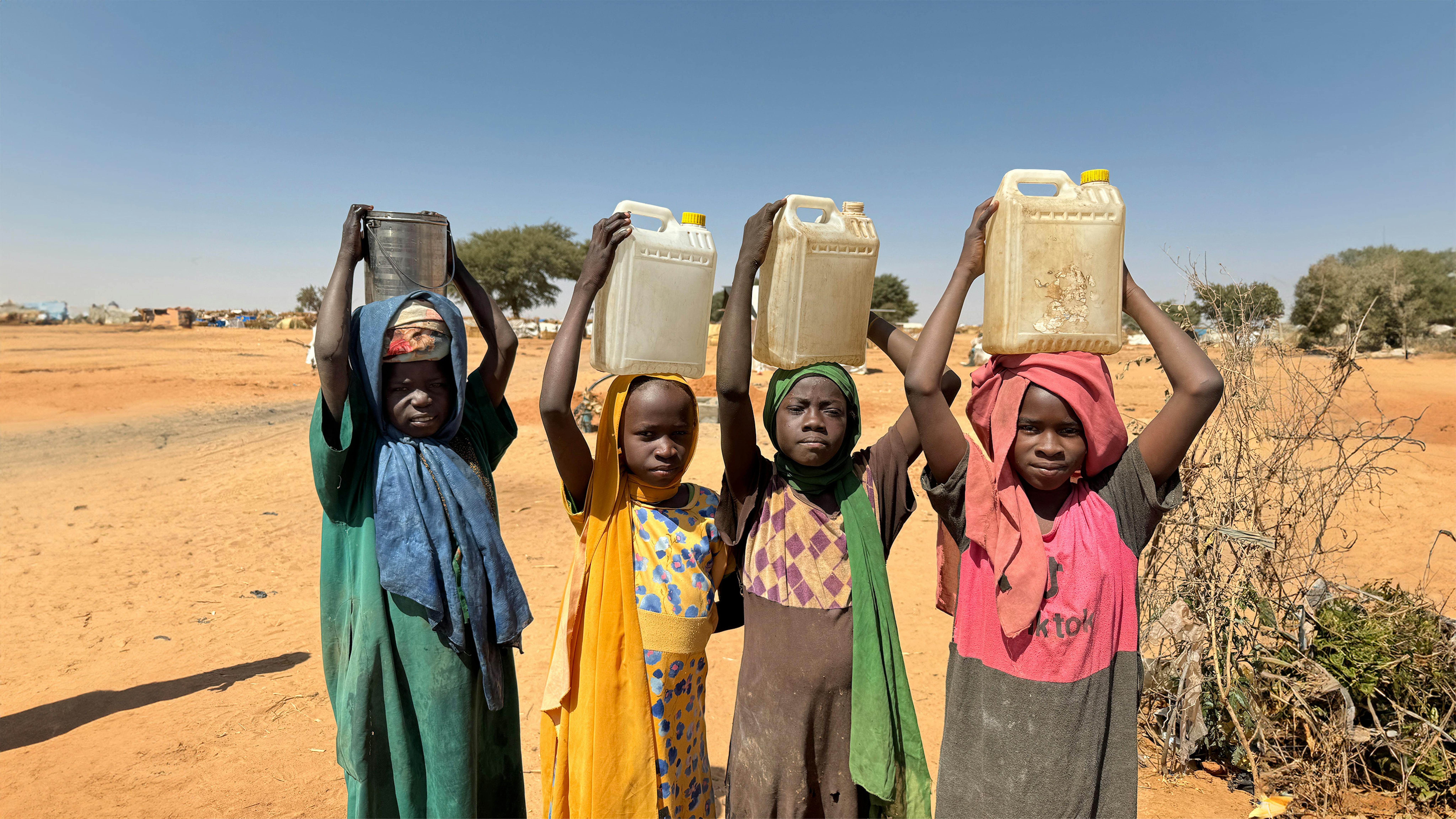 bambini trasportano contenitori d'acqua dopo averli riempiti in un pozzo dell'UNICEF all'interno dell'insediamento di rifugiati di Adré in Ciad.