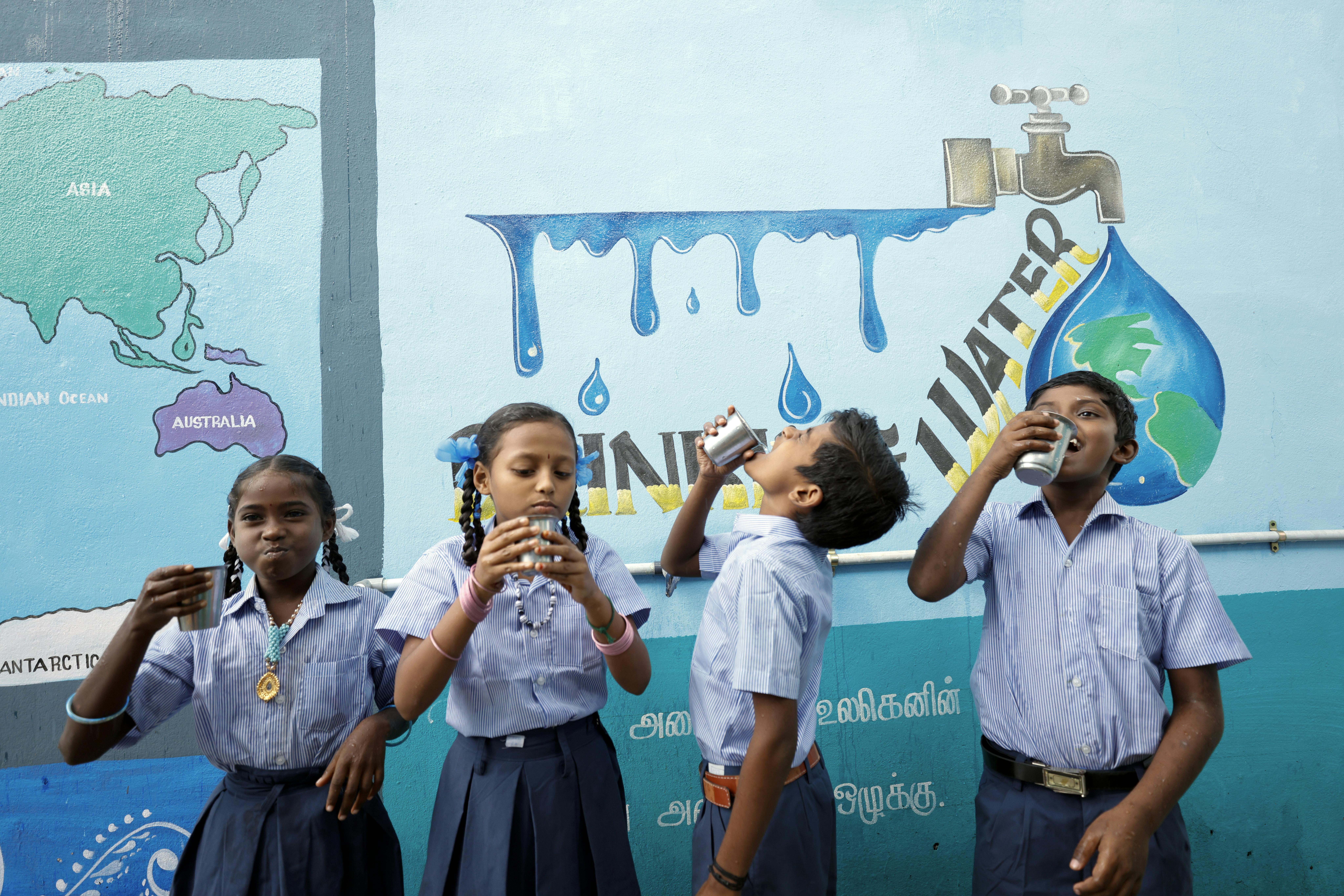 Bambini bevono acqua davanti ad un murales, in India