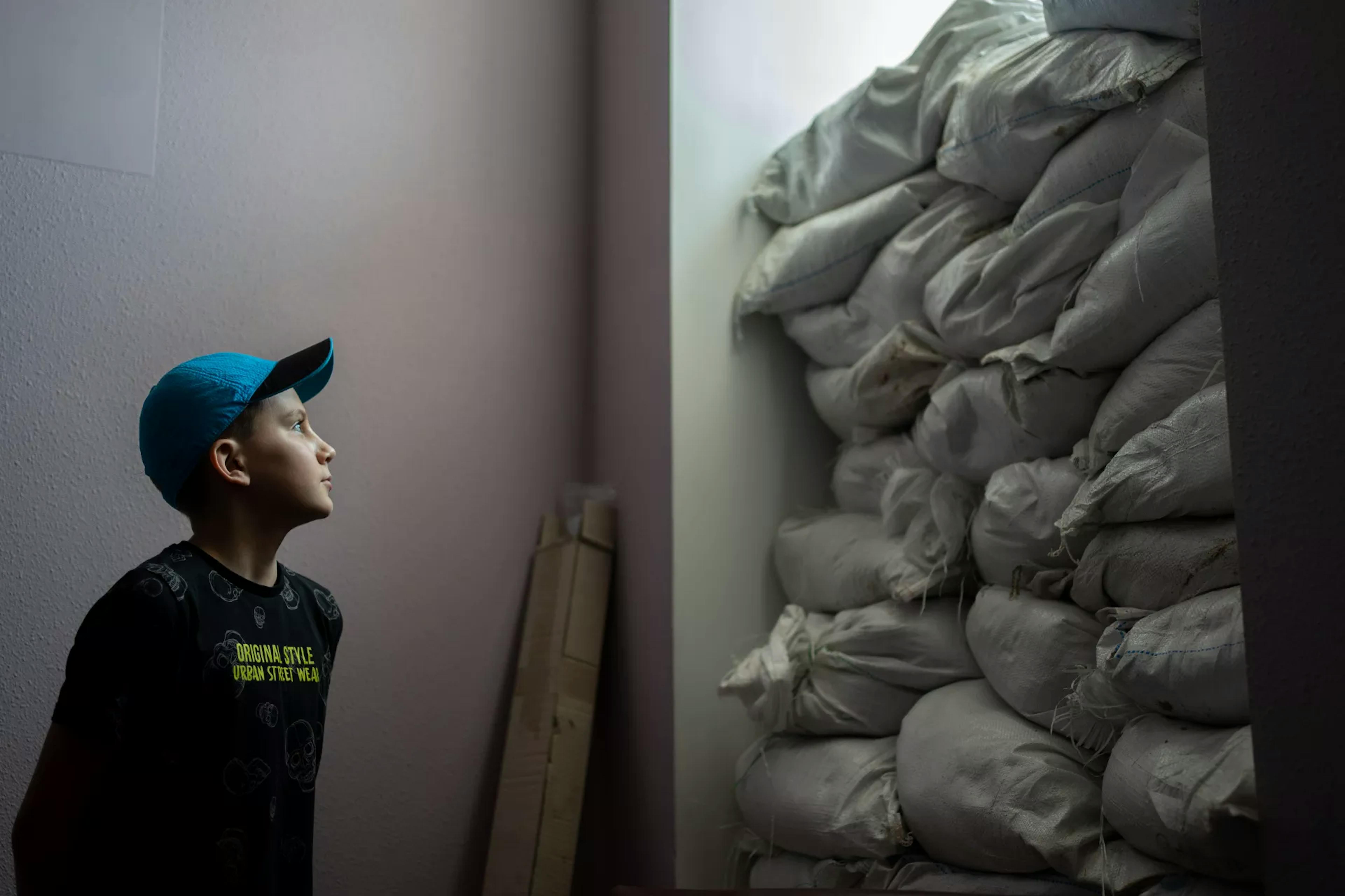Ucraina, un bambino guarda la finestra isolata da sacchi di sabbia per proteggerlo dalle schegge