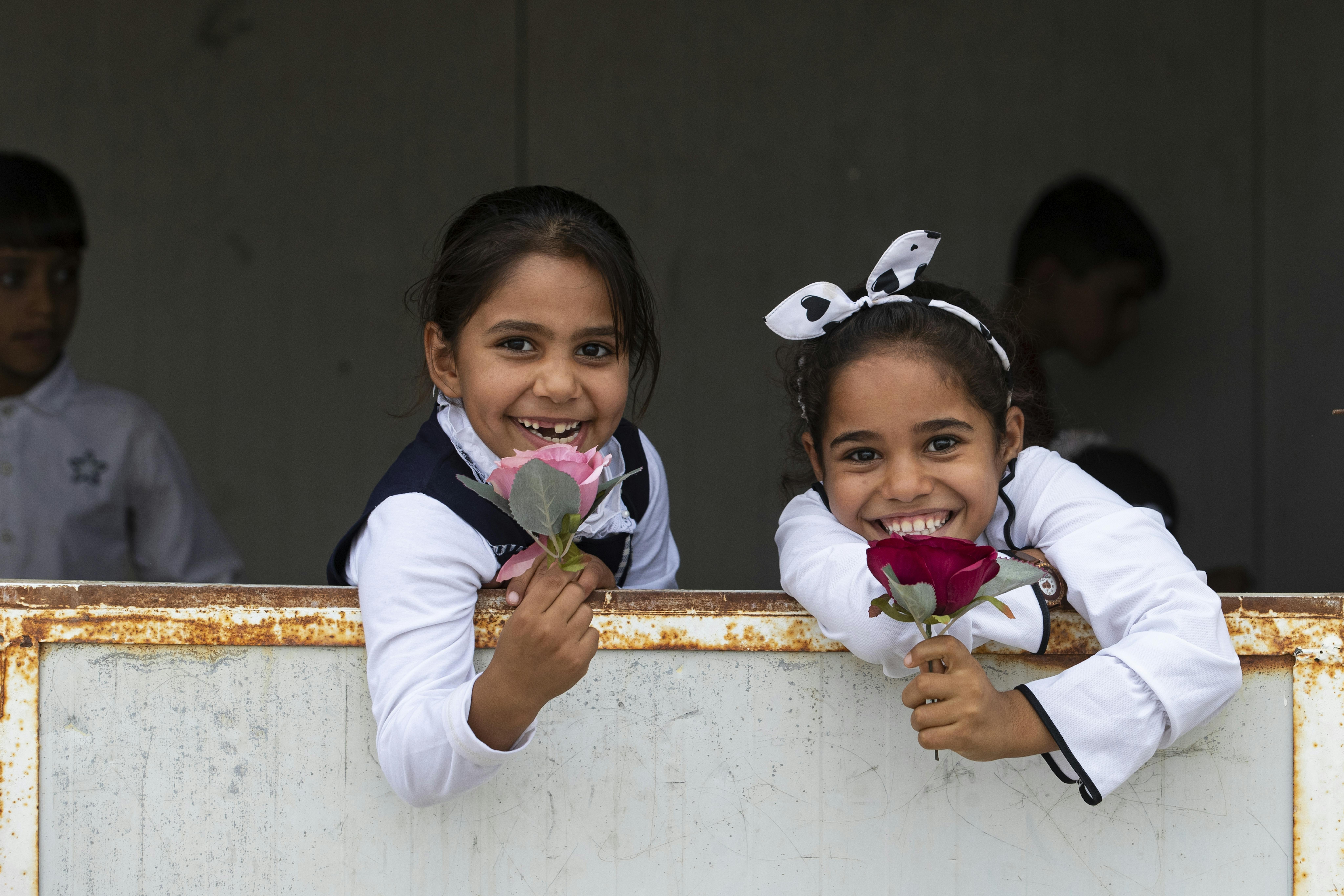 Bambine irachene sorridono, tenendo in mano delle rose