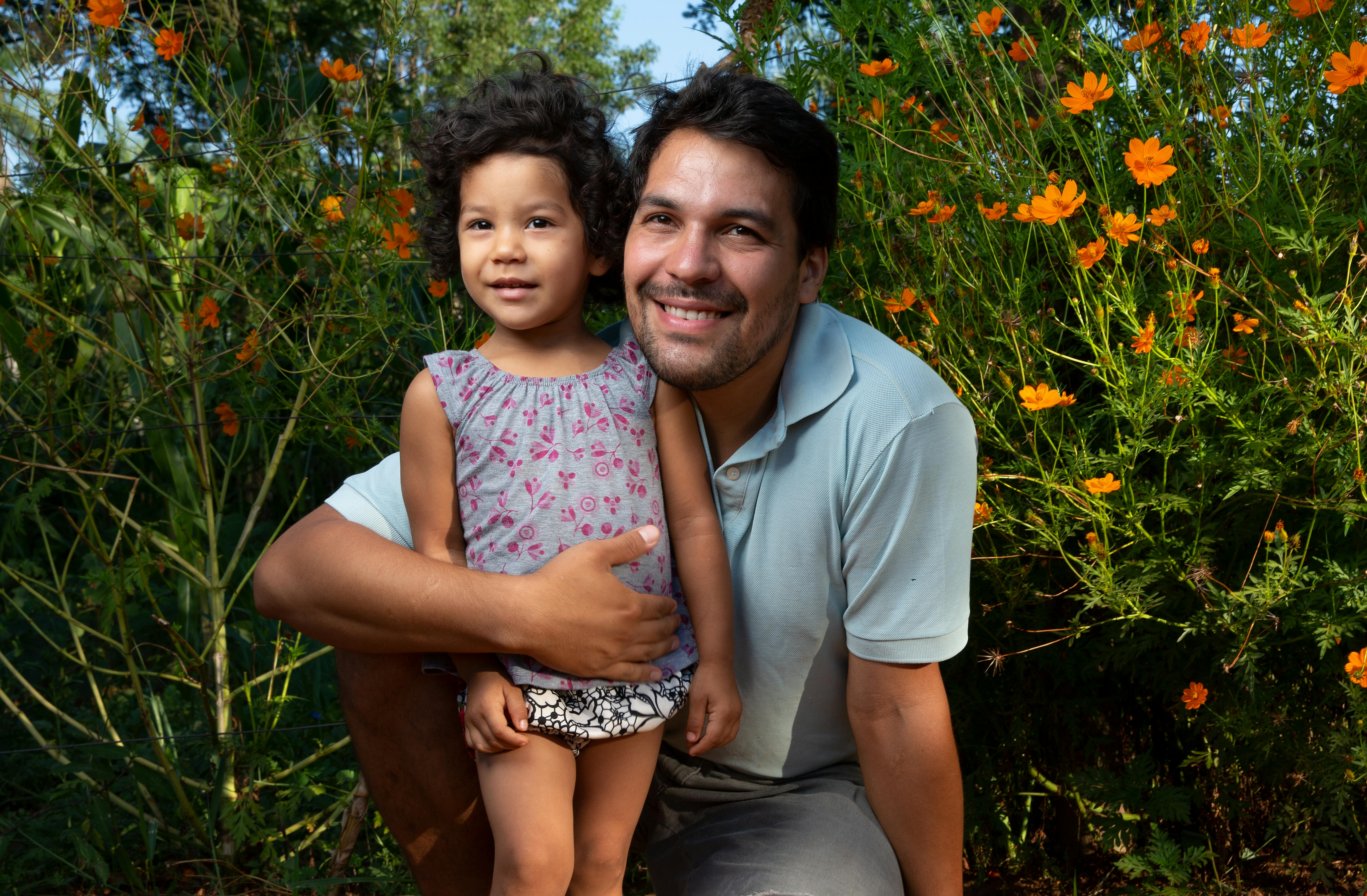 Padre e figlia sorridono, sullo sfondo un prato fiorito