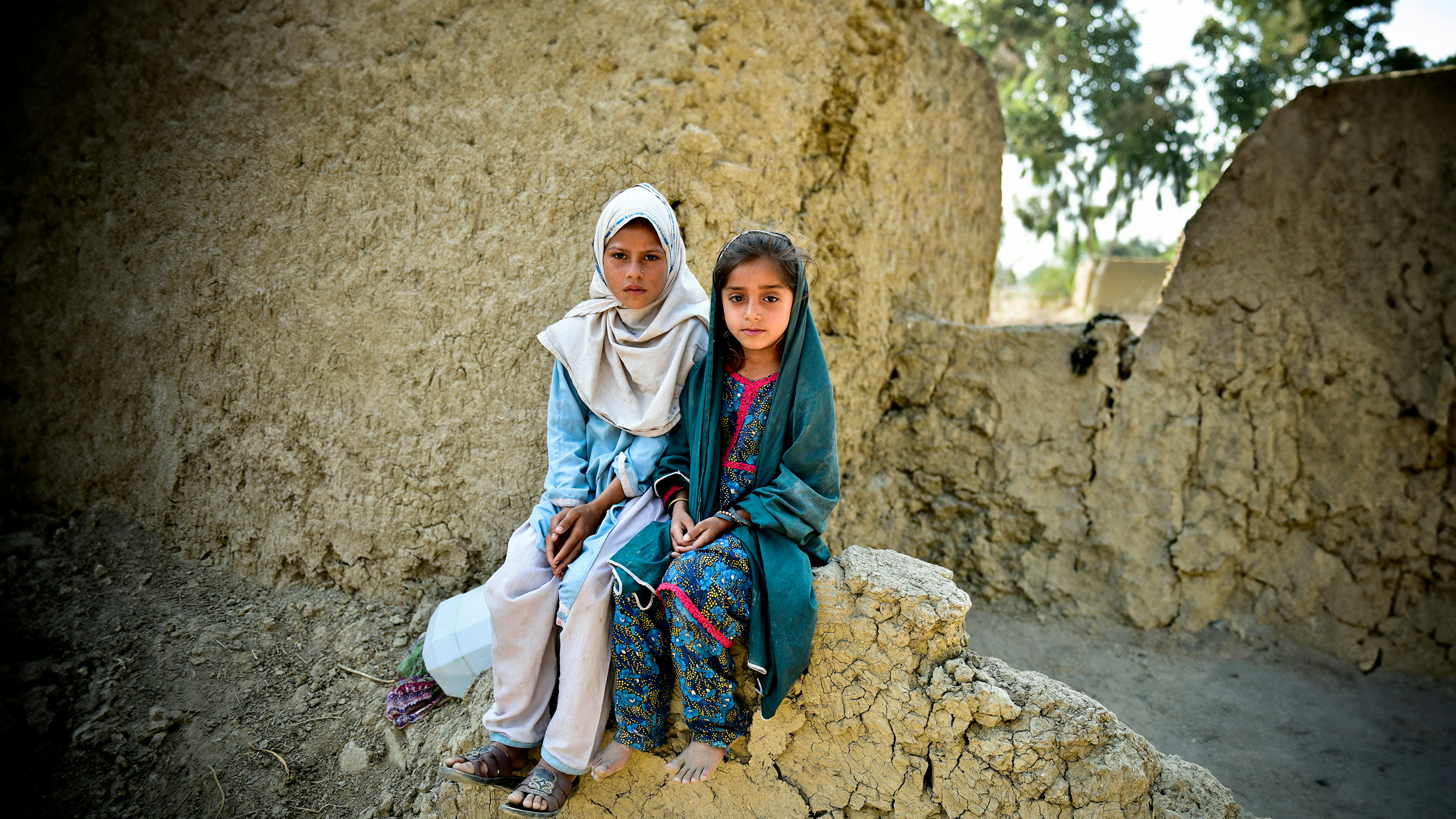 Pakistan - Muriko Bibi (7) e Tehseen (6) siedono sul muro danneggiato della loro casa di fango, quasi distrutta durante le inondazioni del 2022 i