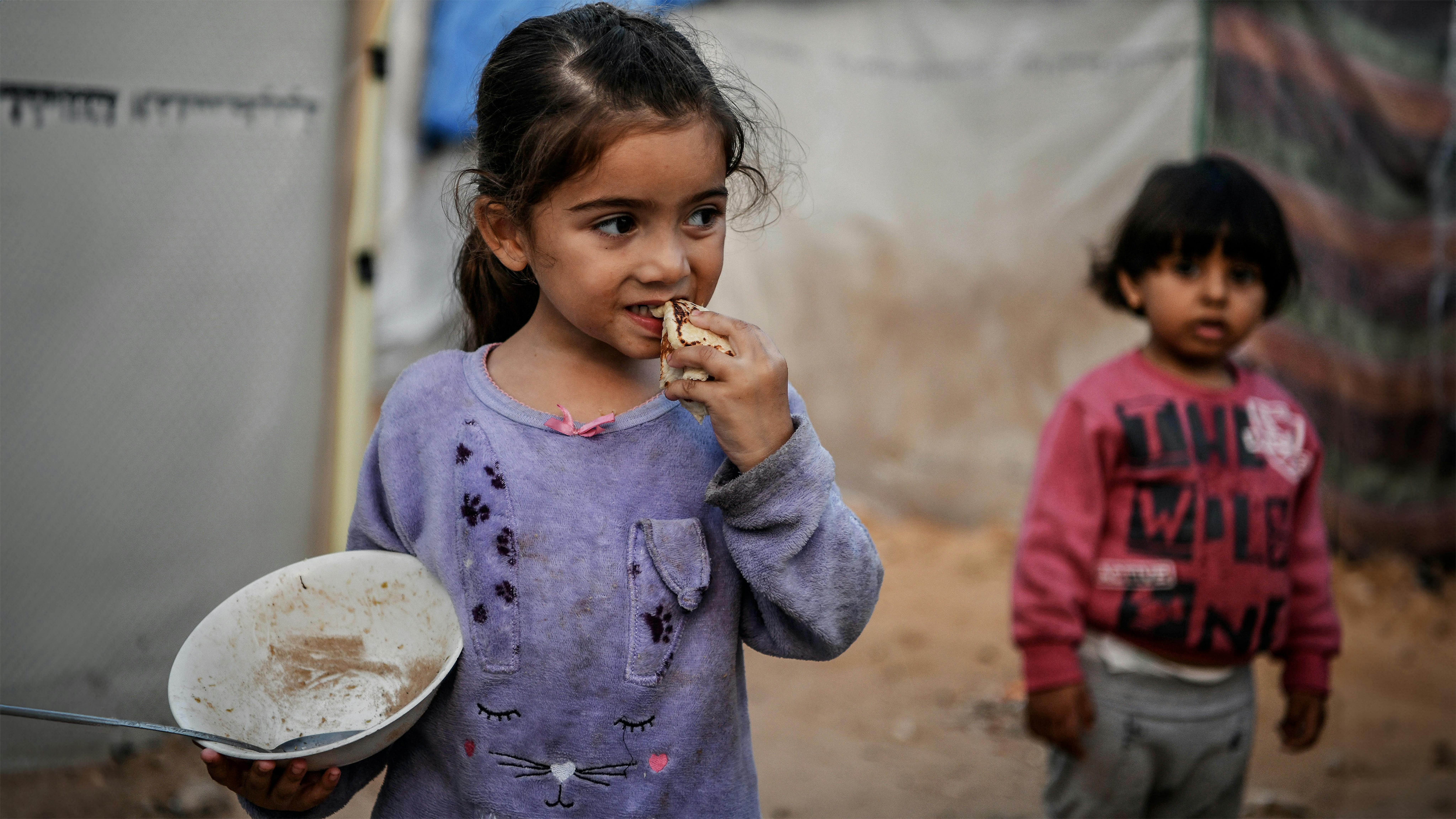 Striscia di Gaza - Israa, una bambina di 3 anni, mangia un pezzo di pane mentre sta davanti alla tenda della sua famiglia nella città di Khan Younis,