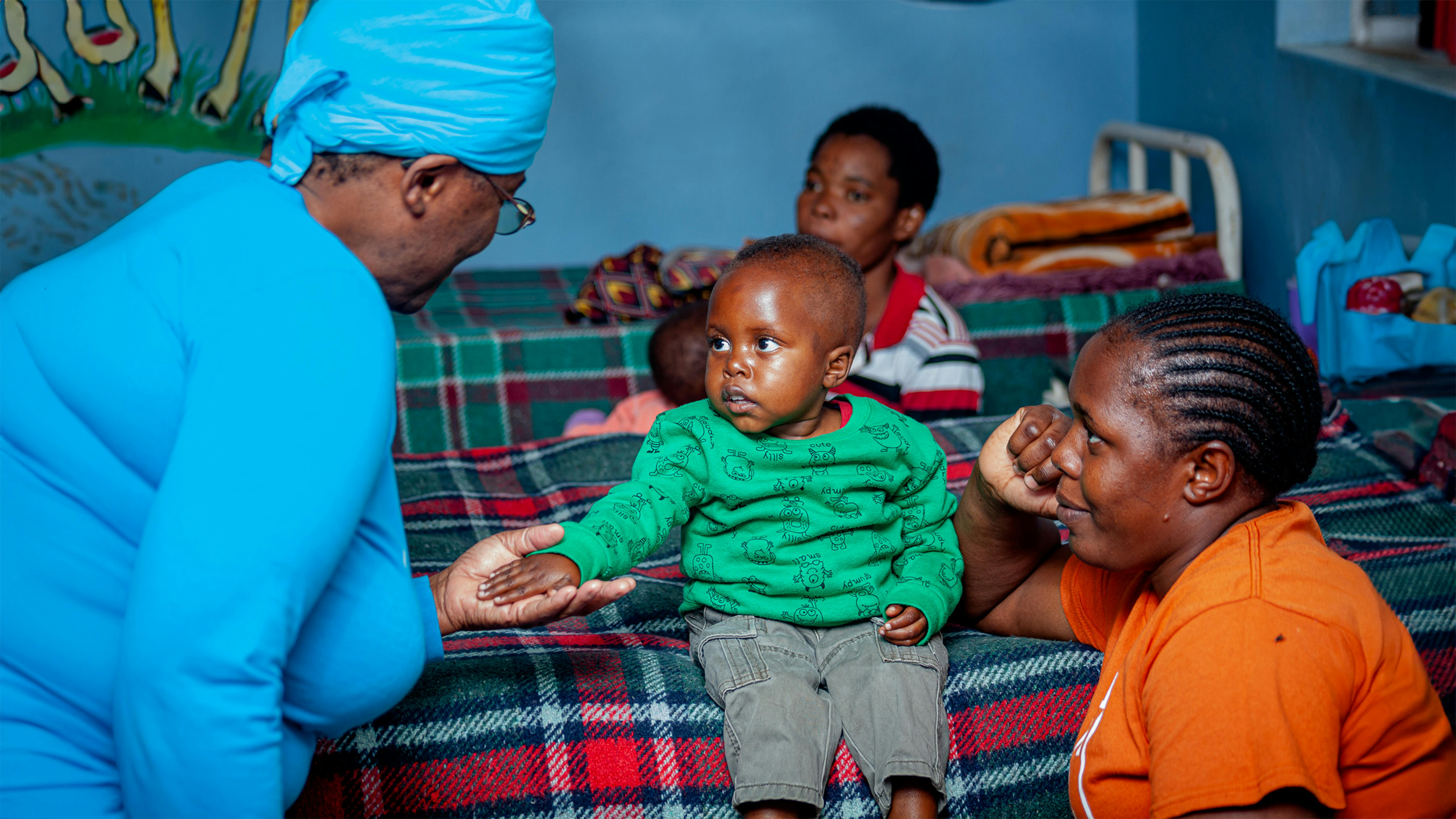 Zambia, Betty Chella Nalungwe (a sinistra), comunication officer  dell'UNICEF Zambia, parla con una madre e un bambino durante  la visita di una delegazione dell'UNICEF  al reparto di degenza di Monze Mission Hospital per vedere come vengono trattati i bambini sotto i 5 anni per la malnutrizione