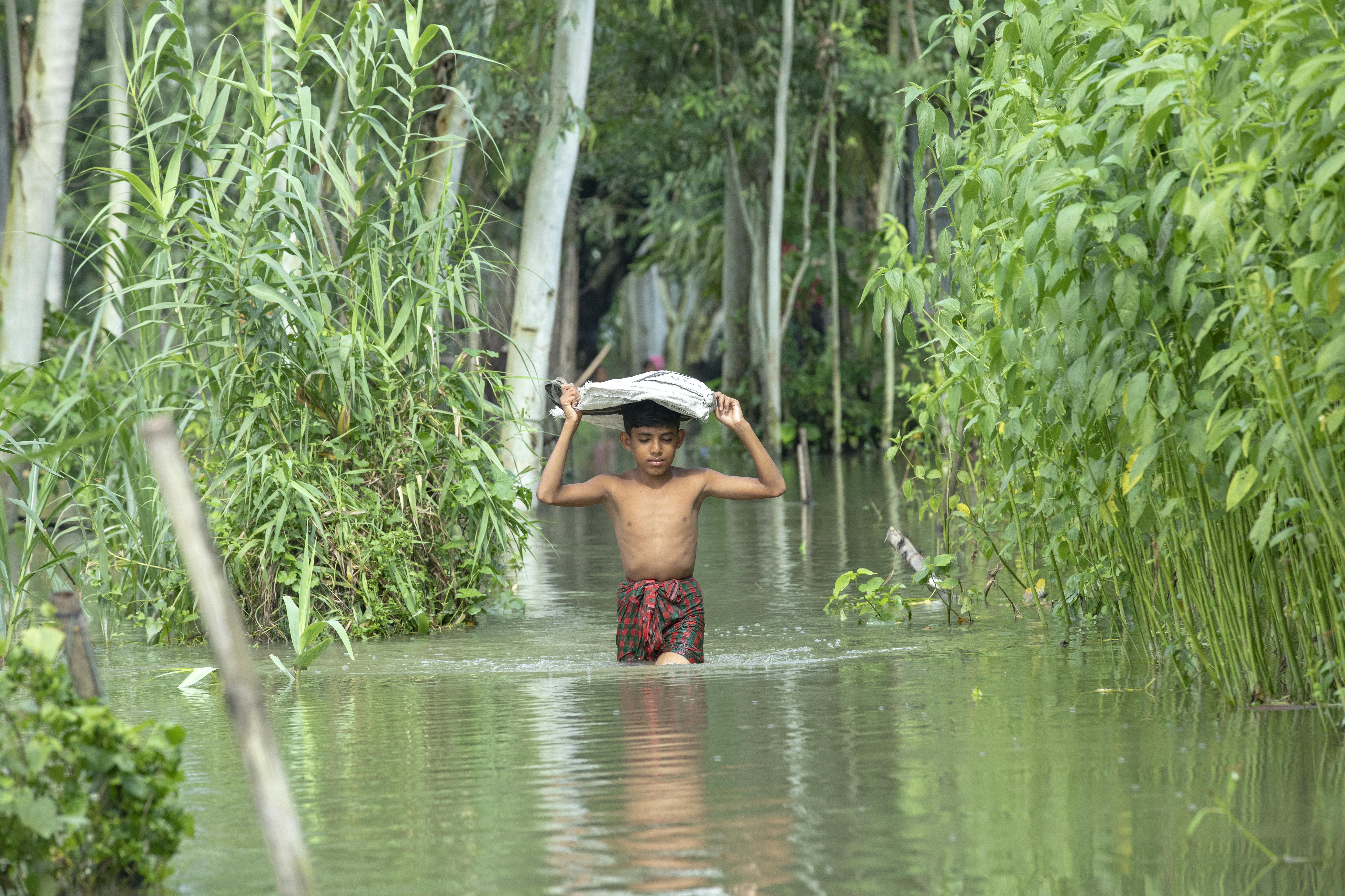 Bambino trasporta sacco di riso nell'acqua, bangladesh, alluvione