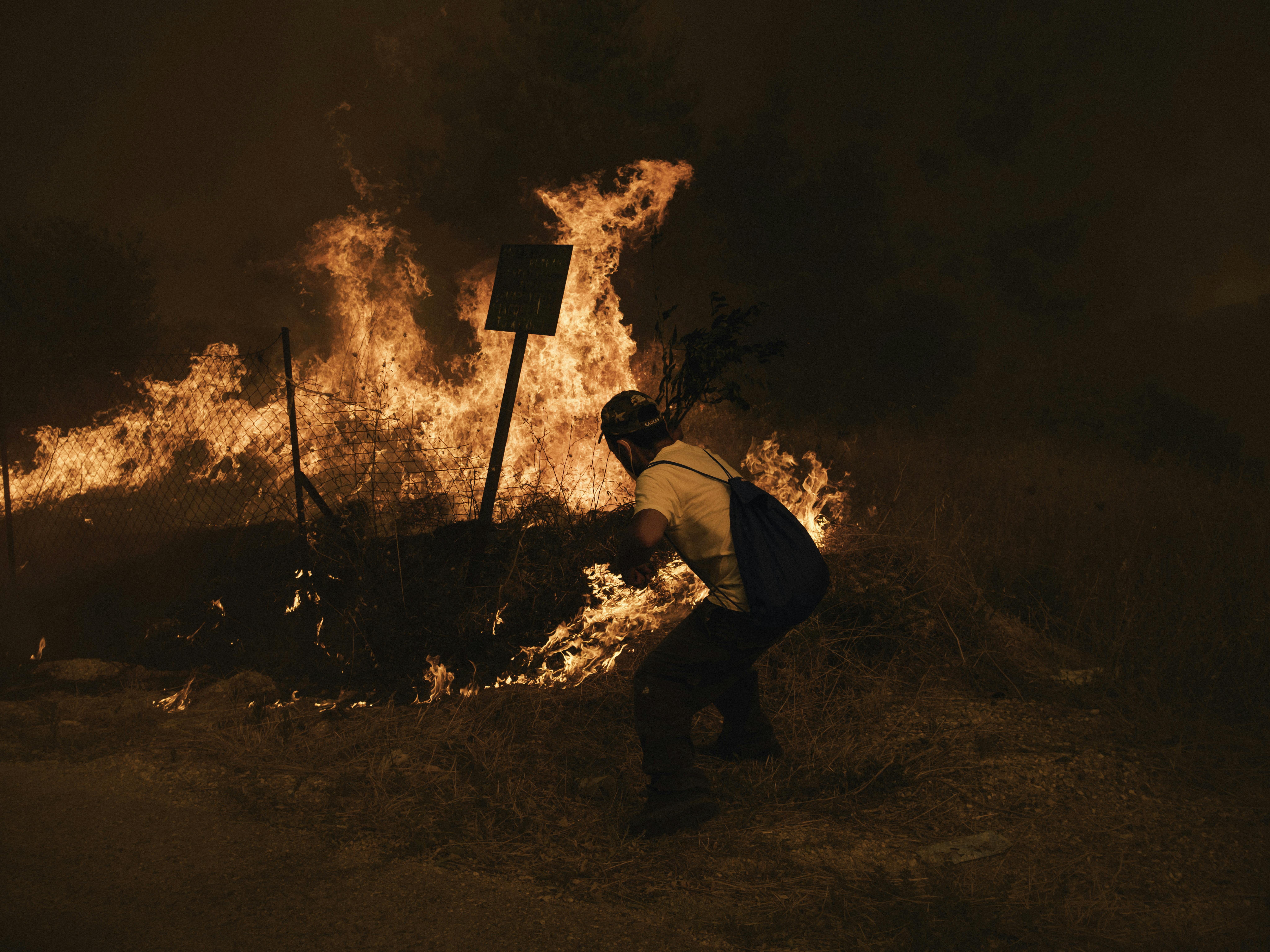 Un uomo cerca di spegnere un incendio che si sta avvicinando alla sua casa ad Afidnes, nella parte nord di Atene