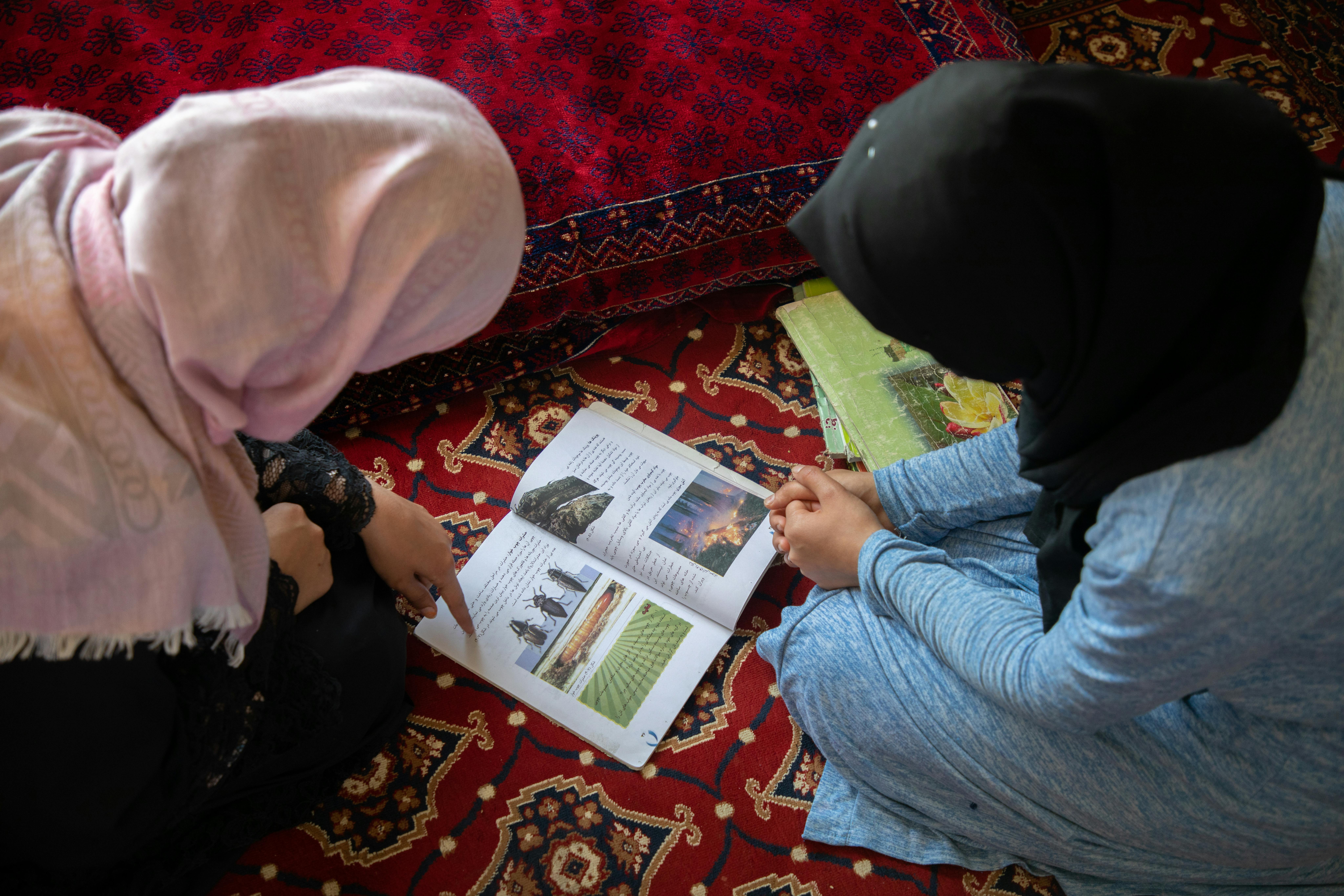 Sharifa* (a sinistra), 15 anni, aiuta la sorella minore Madina*, 13 anni (a destra) con gli studi. Entrambe sono fuori dalla scuola da quasi tre anni. in Afghanistan alle ragazze non è più permesso studiare