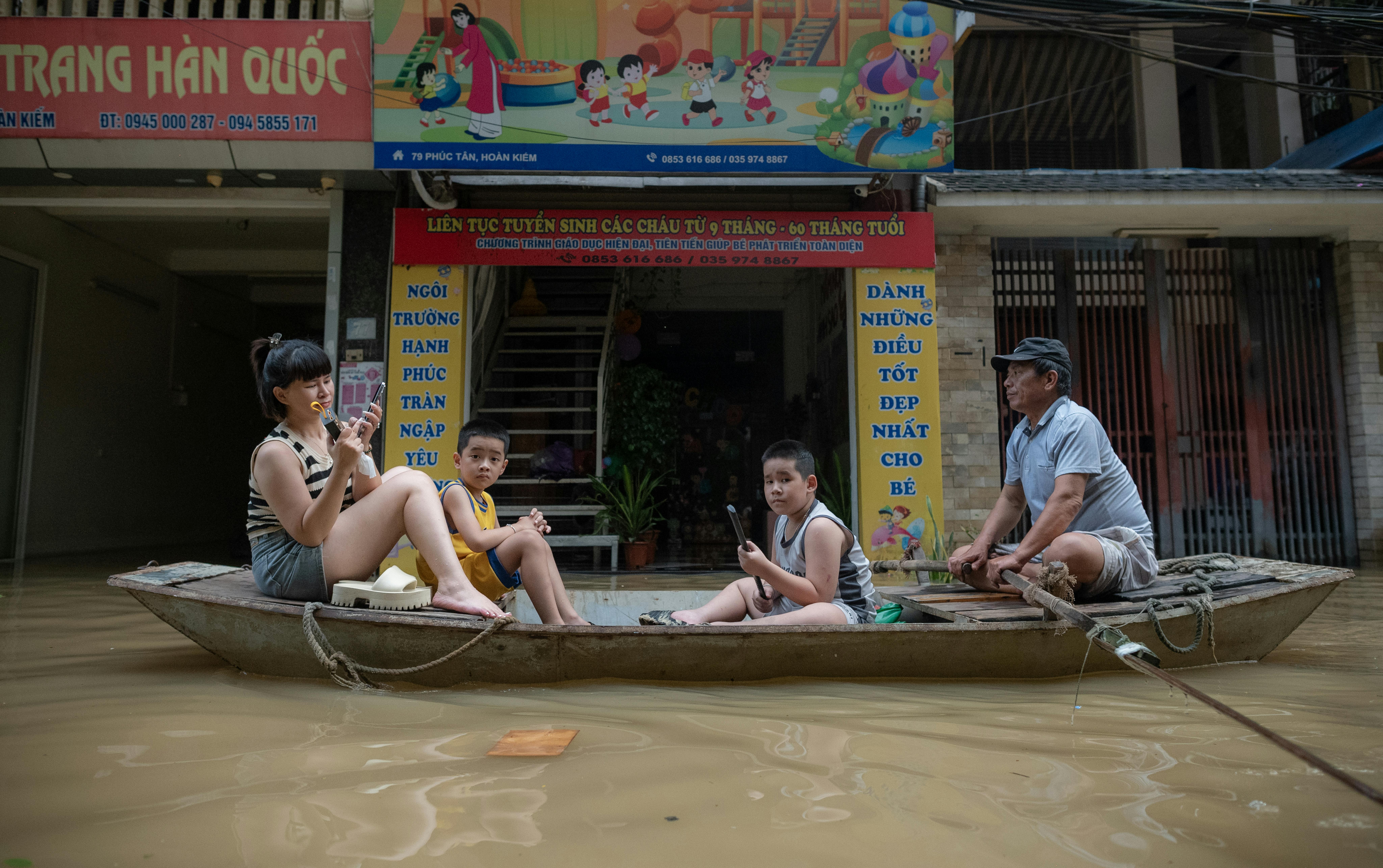 Una mamma con i suoi due figli tornano a casa passando davanti all'asilo Anh Sao, ad Hanoi, allagato a causa del tifone
