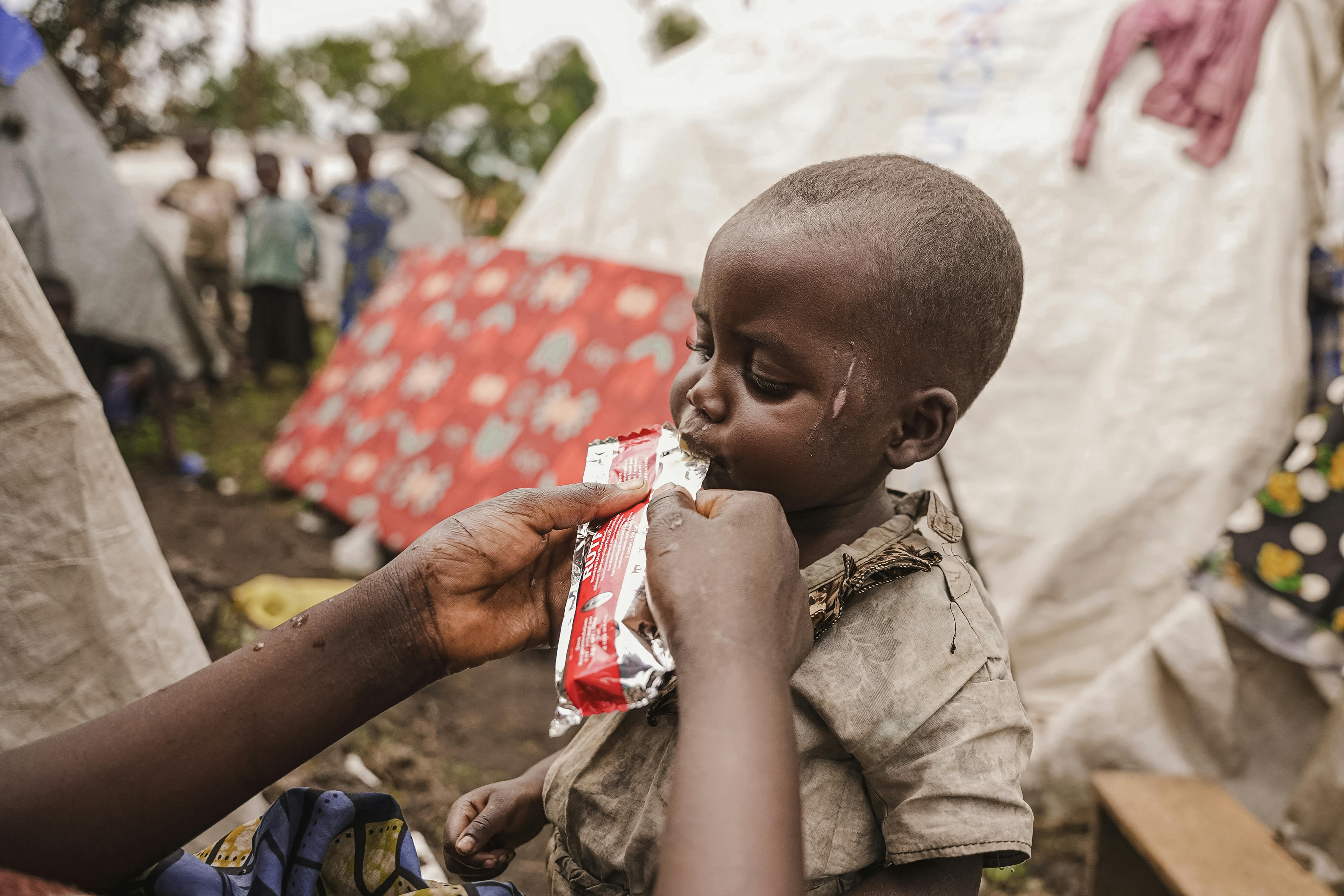 Rep. Democratica del Congo: Marie somministra a sua figlia Furaha una bustina di RUTF, nel campo profughi dove vivono.  L’UNICEF e i suoi partner lavorano nel campo sfollati ad una vasta campagna di screening sulla malnutrizione