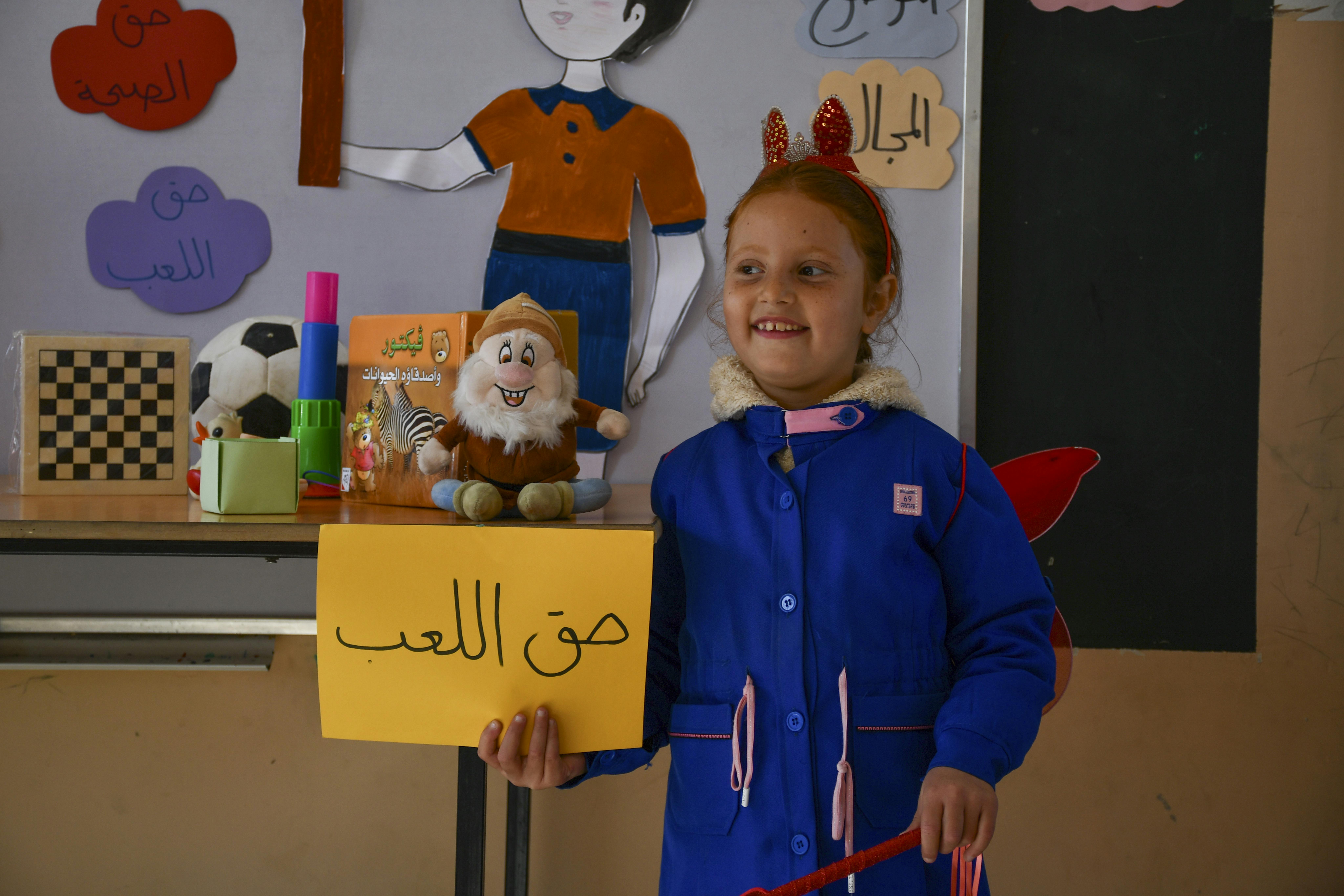 Najwa, 8 anni, presenta un cartello che rappresenta il diritto al gioco durante la celebrazione della Giornata mondiale dei bambini nella sua scuola nel villaggio di Mahmadiyeh