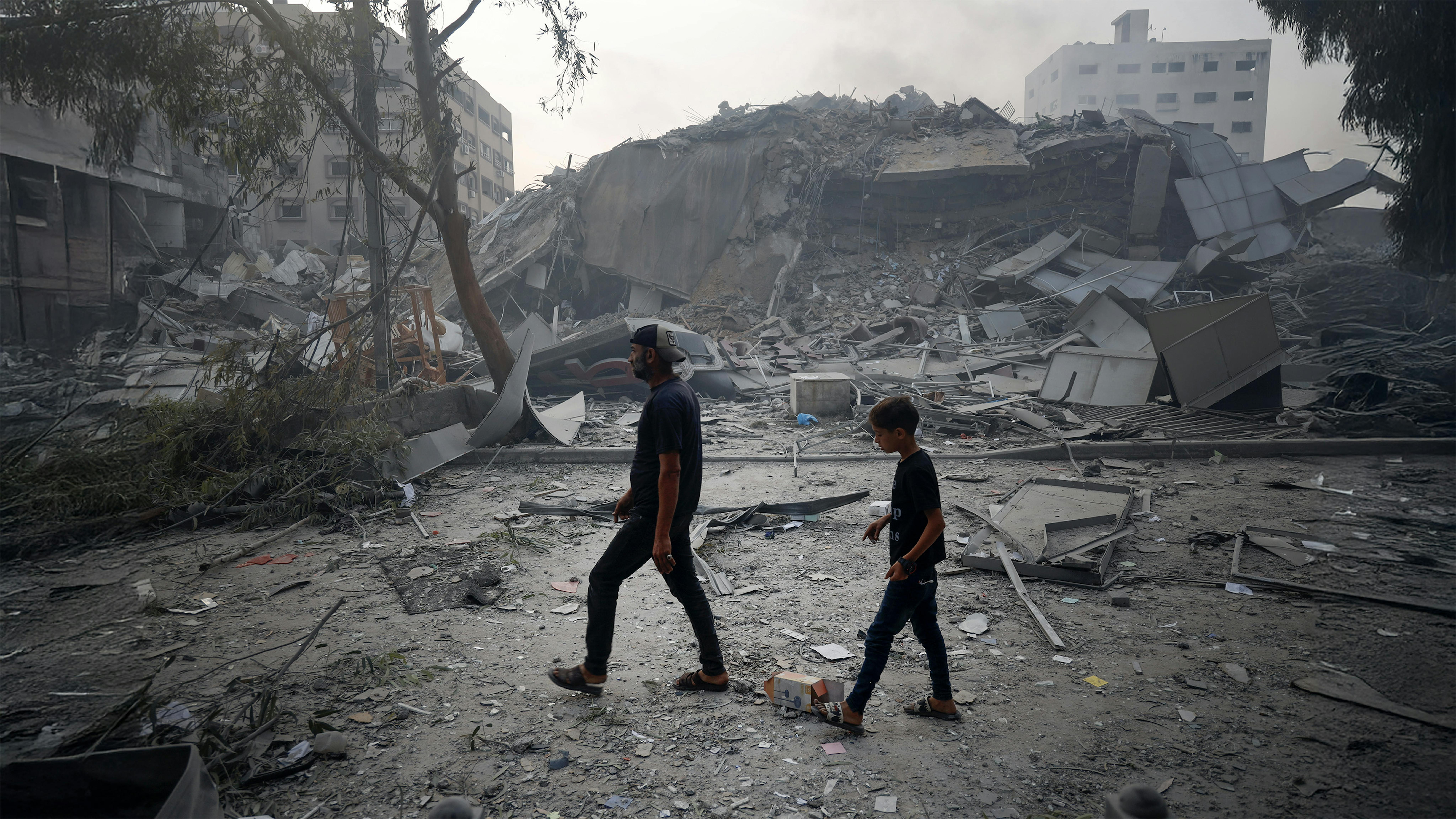 Un bambino e suo padre mentre passano tra le macerie degli edifici di Gaza City.