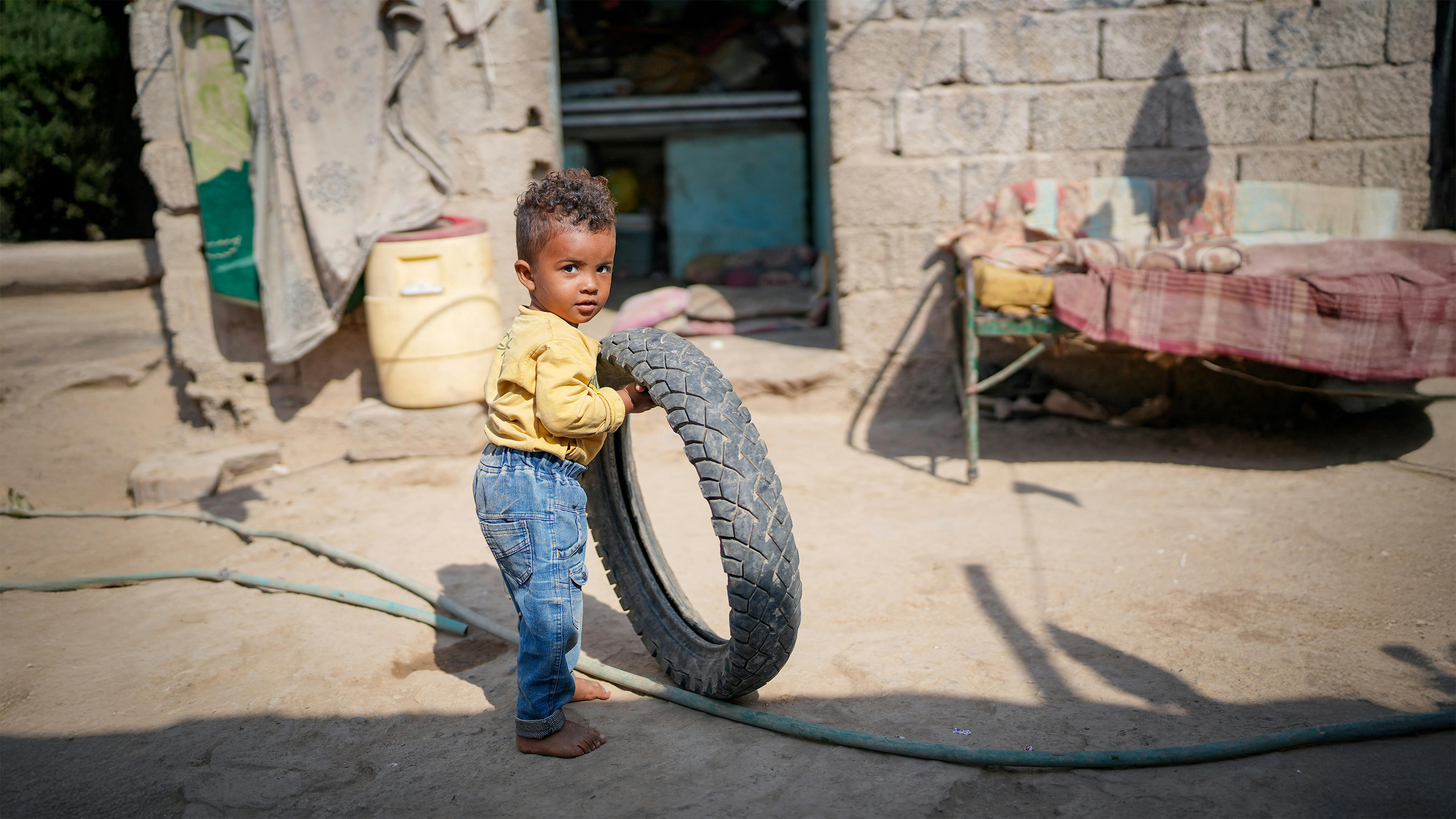 Il bambino Sand, guarito dalla malnutrizione, gioca con una vecchia ruota di bicicletta nel suo cortile a Lahj, nello Yemen.