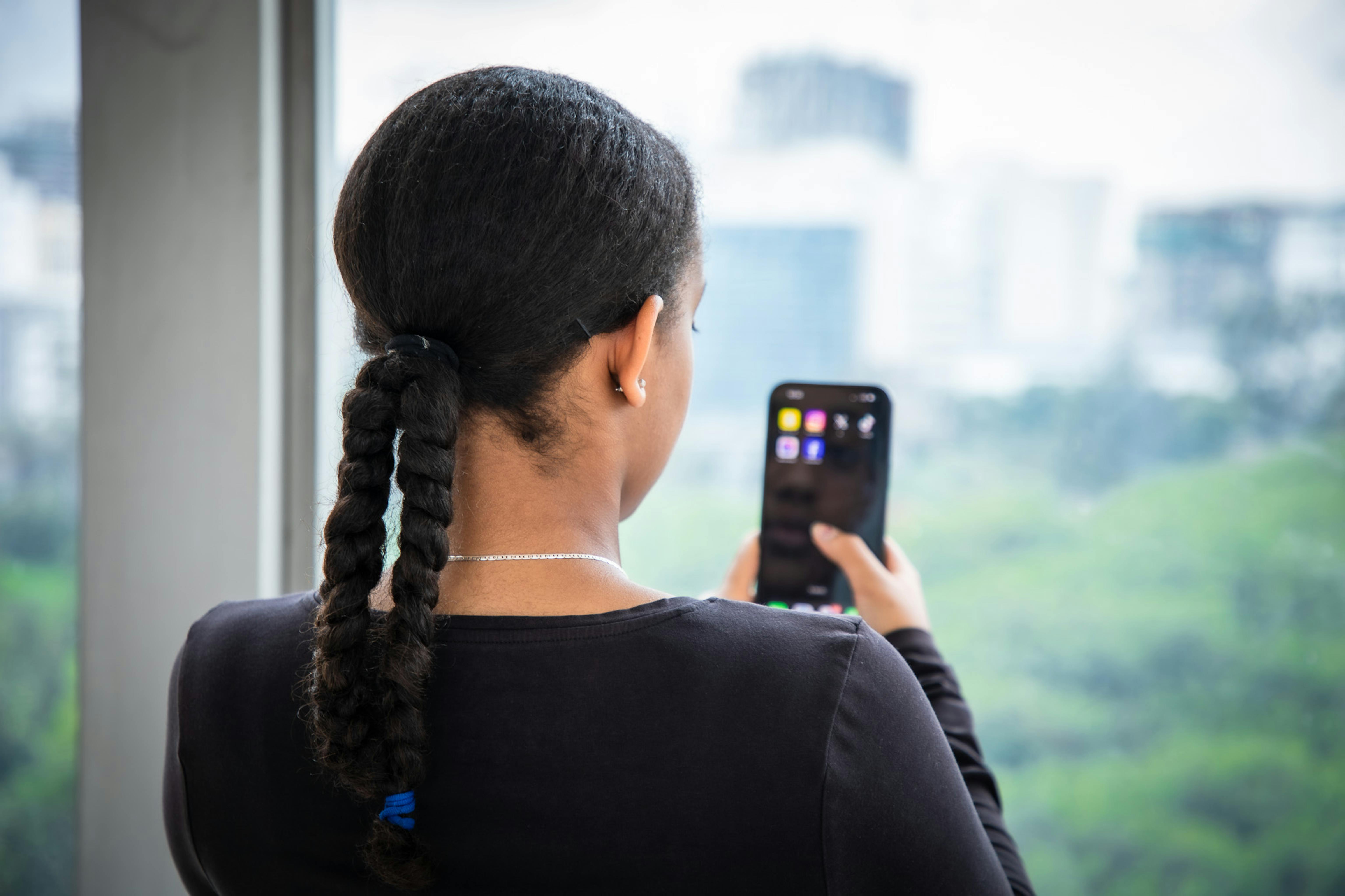 Crescere online offre opportunità illimitate ma anche seri rischi come l'esposizione a contenuti violenti, la violazione della propria privacy e il cyberbullismo. Questa ragazza osserva lo smartphone affacciata a una finestra