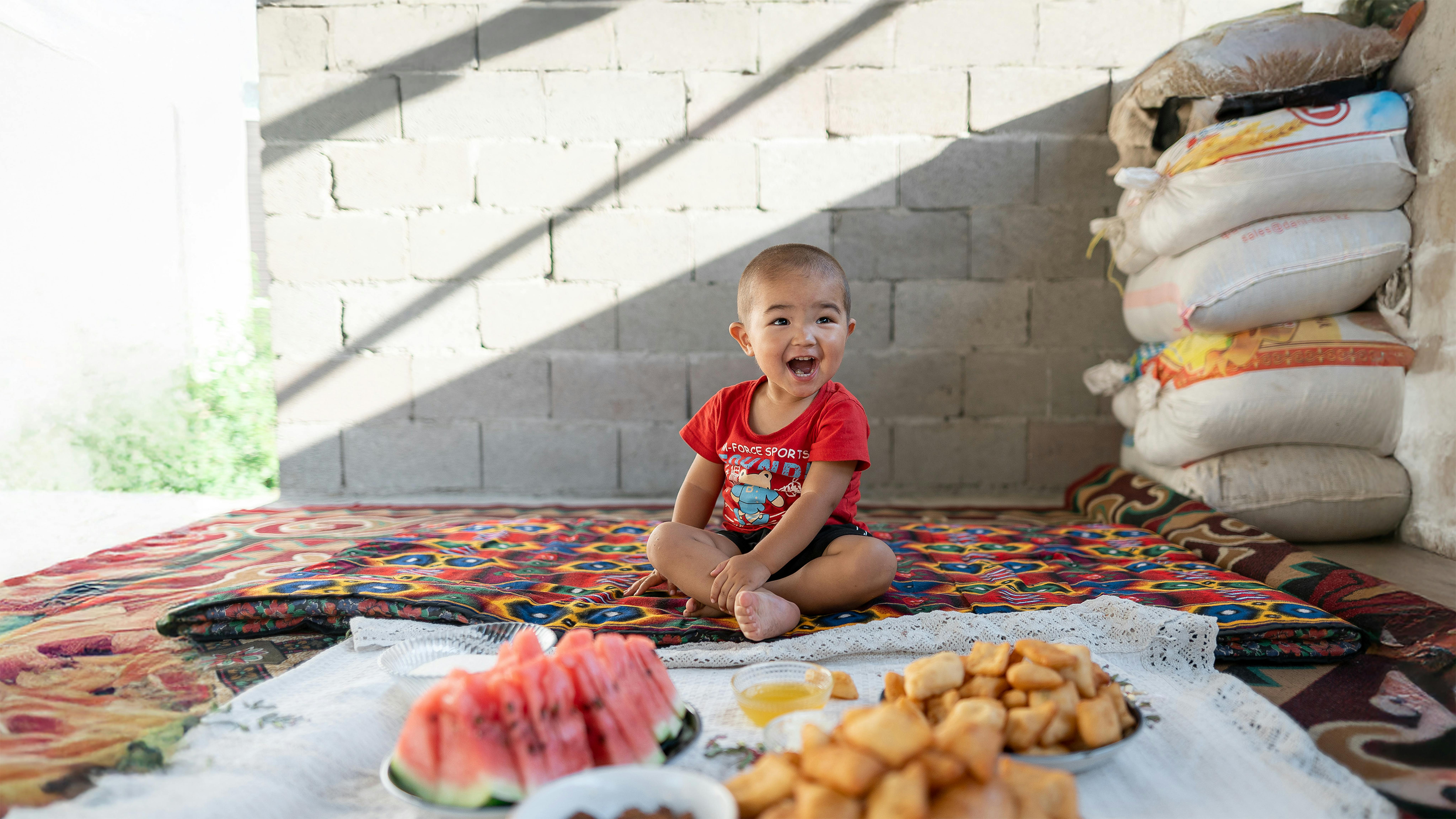 Ariet, 2 anni, si siede per terra con alcuni dei suoi cibi preferiti, a casa nel villaggio di Kurshab, Oblast', Kirghizistan