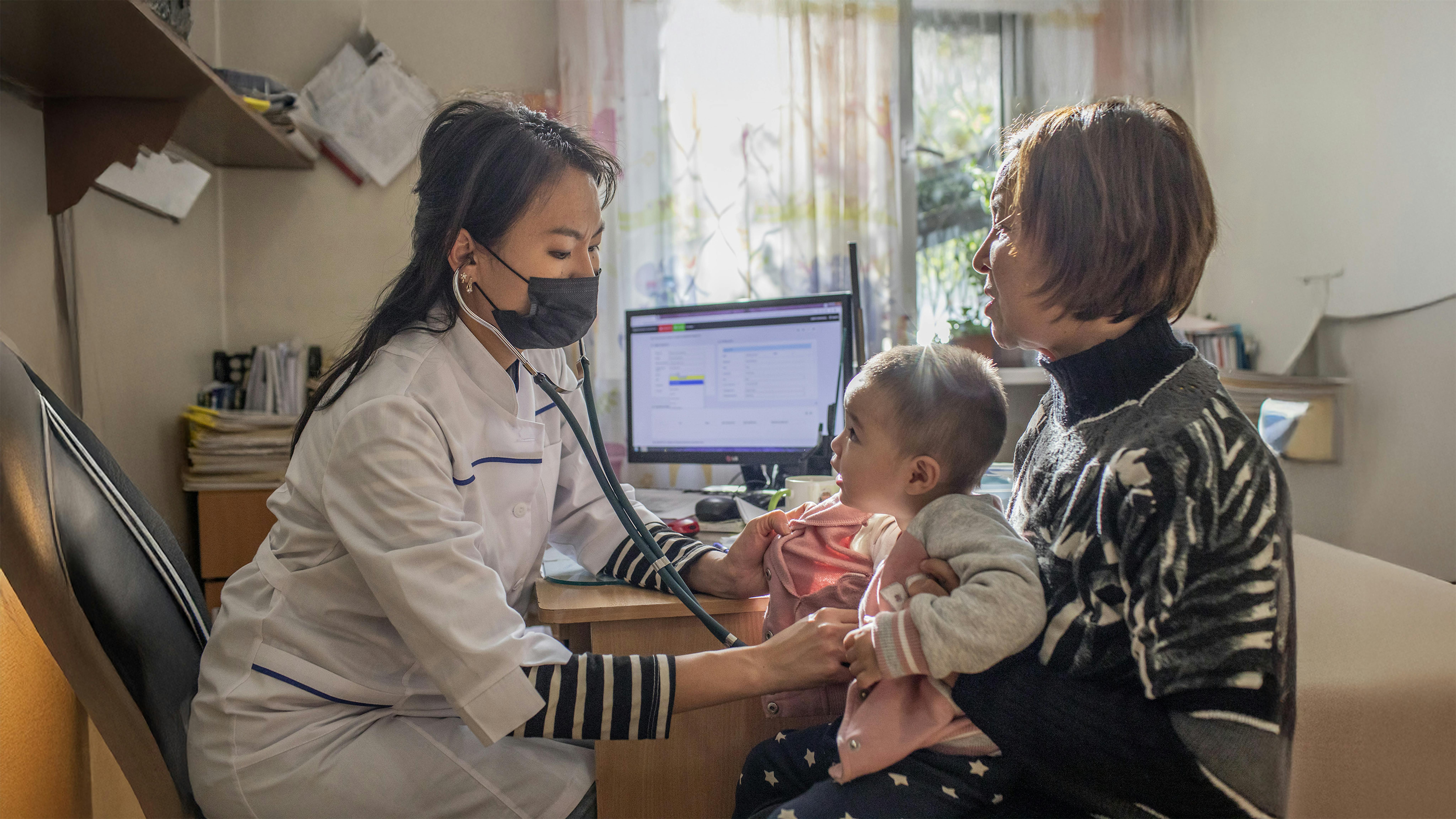 Kirghizistan, Cholpon Makkanbaeva, 62 anni, tiene in braccio sua nipote, Emilia Ismanova di 18 mesi, mentre viene visitata dalla pediatra Aidana Askarova presso il Centro di Medicina di Famiglia numero 7 a Bishkek.