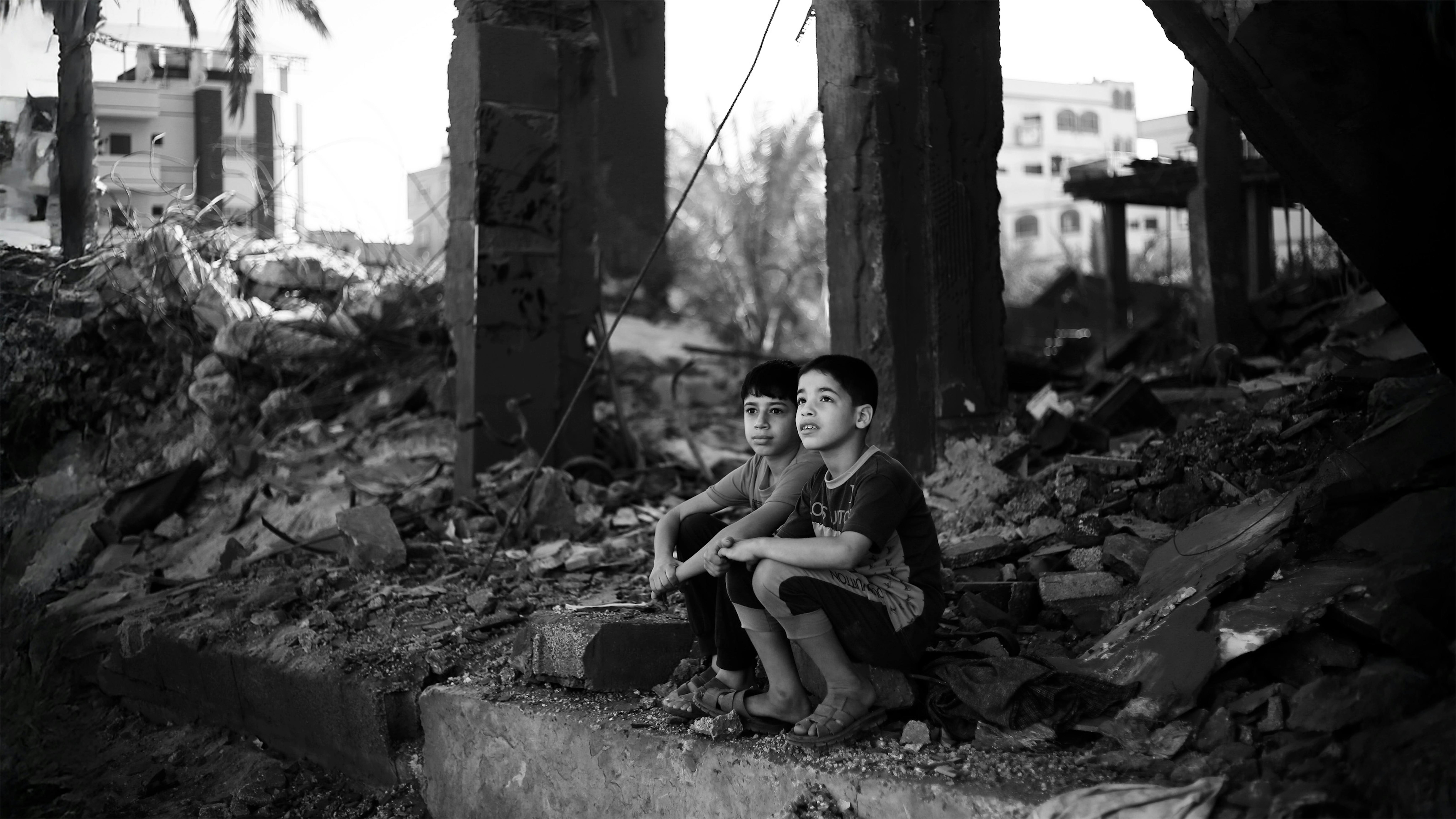 Due bambini palestinesi seduti tra le macerie di ciò che resta della loro casa nella città di Rafah