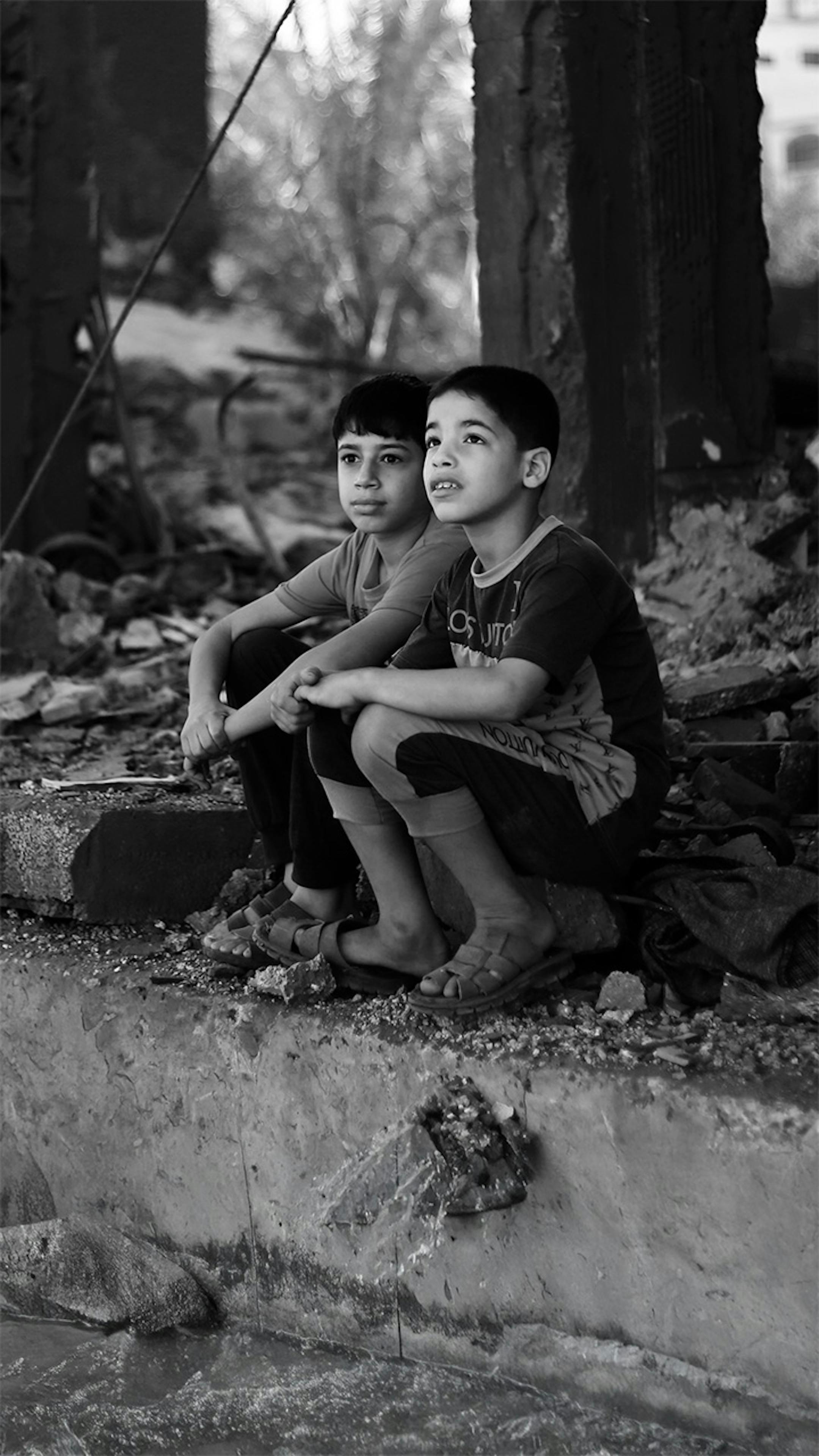 Due bambini palestinesi seduti tra le macerie di ciò che resta della loro casa nella città di Rafah