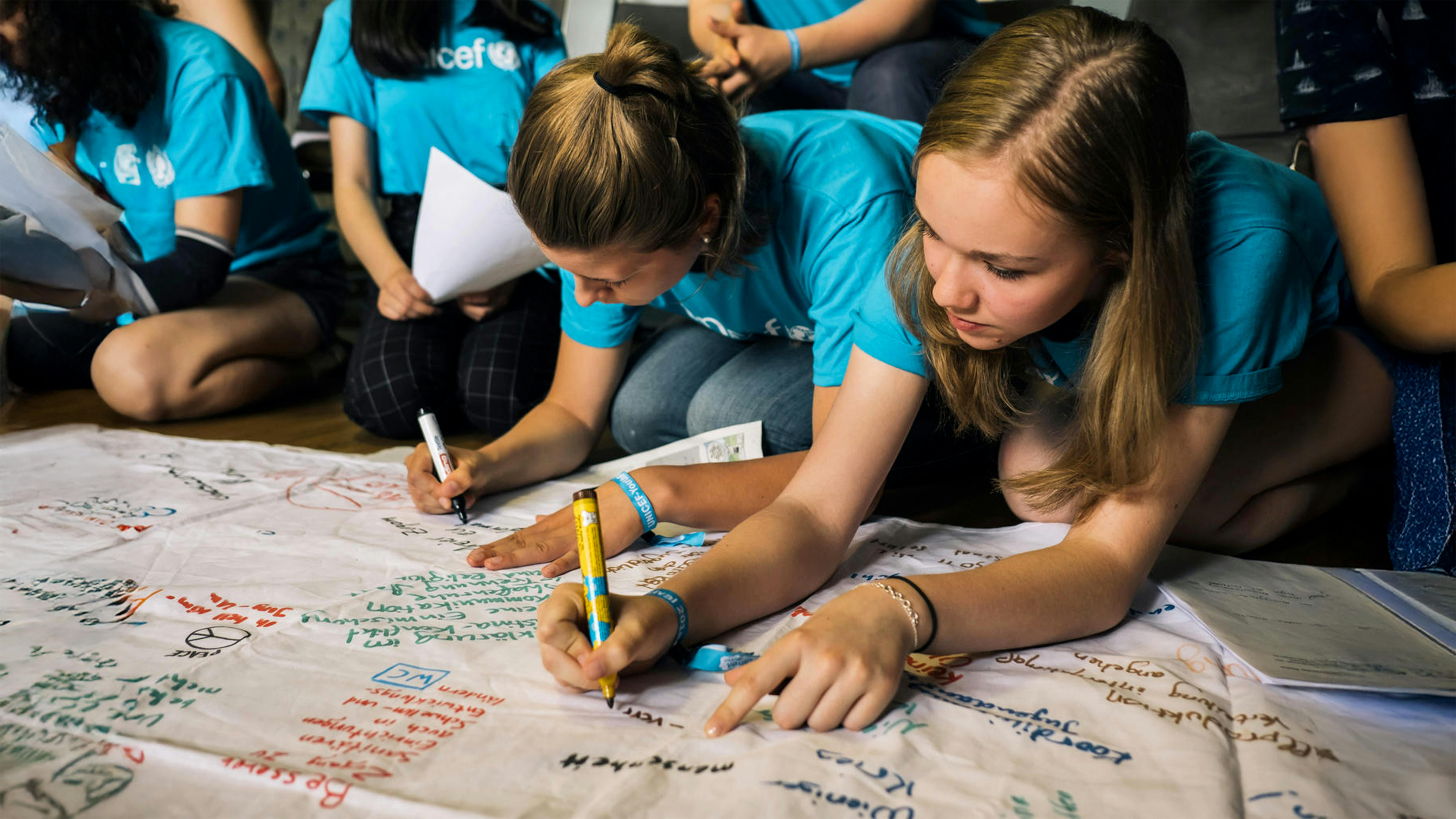 Partecipanti al 2° Festival della Gioventù dell'UNICEF che disegnano su manifesto di stoffa