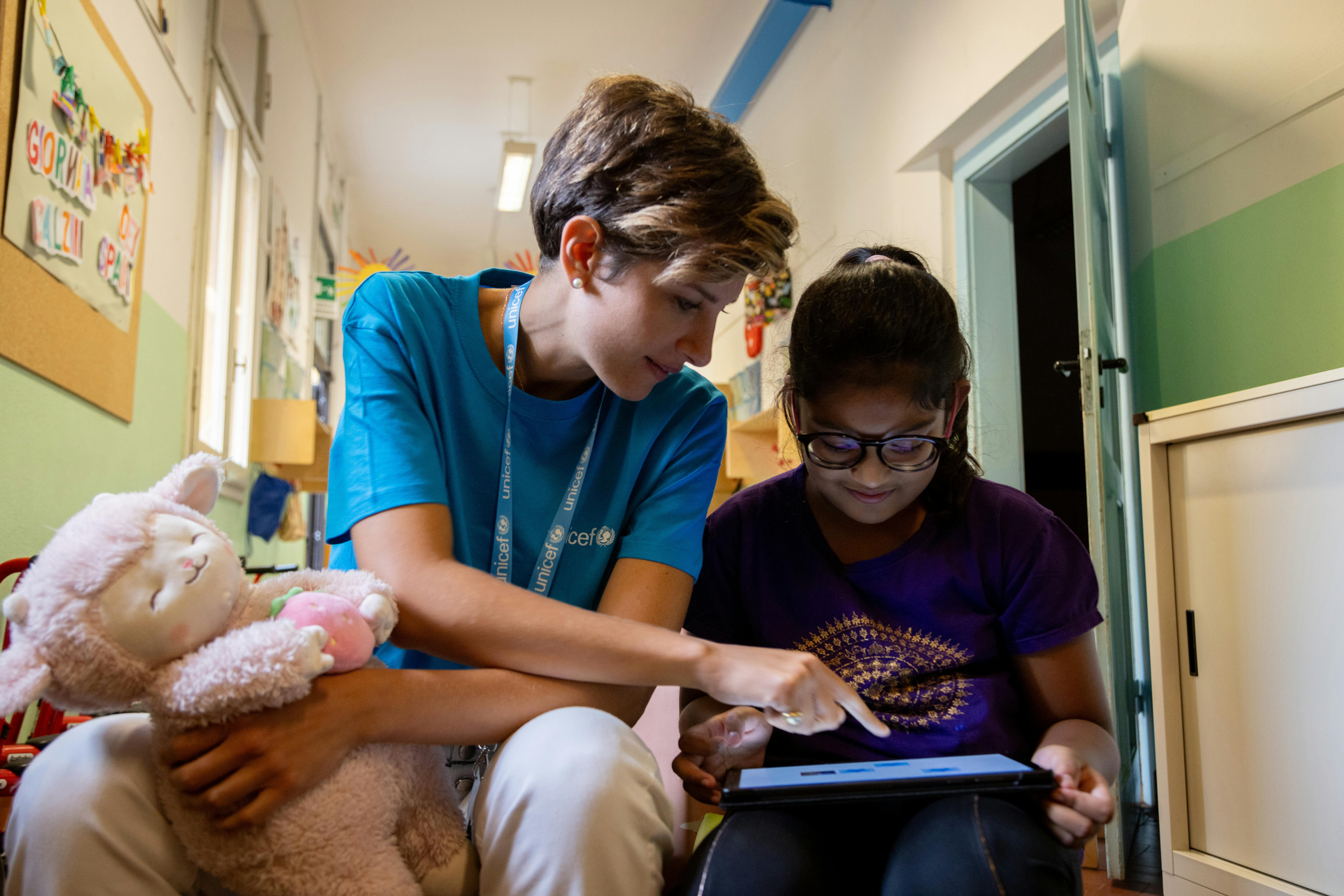 Operatrice UNICEF aiuta una bambina con il tablet. hero corsi online