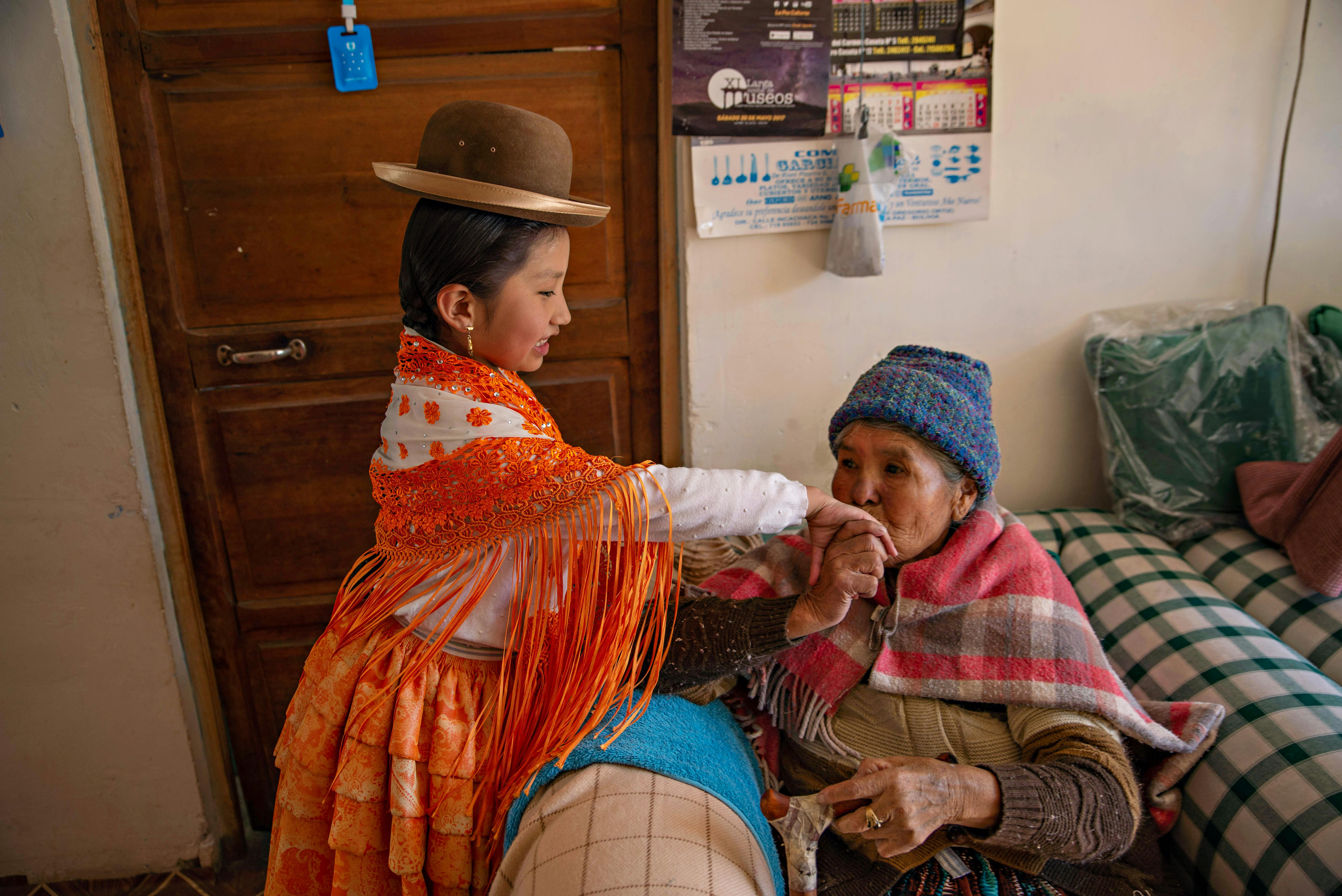 Nonna Rosa dà un bacio alla mano della nipotina, Nathaly. Le donne della famiglia rappresentano quattro generazioni di Cholitas: nome che si riferisce alle donne indigene, in particolare della comunità aymara, riconoscibili per il loro abbigliamento tradizionale,