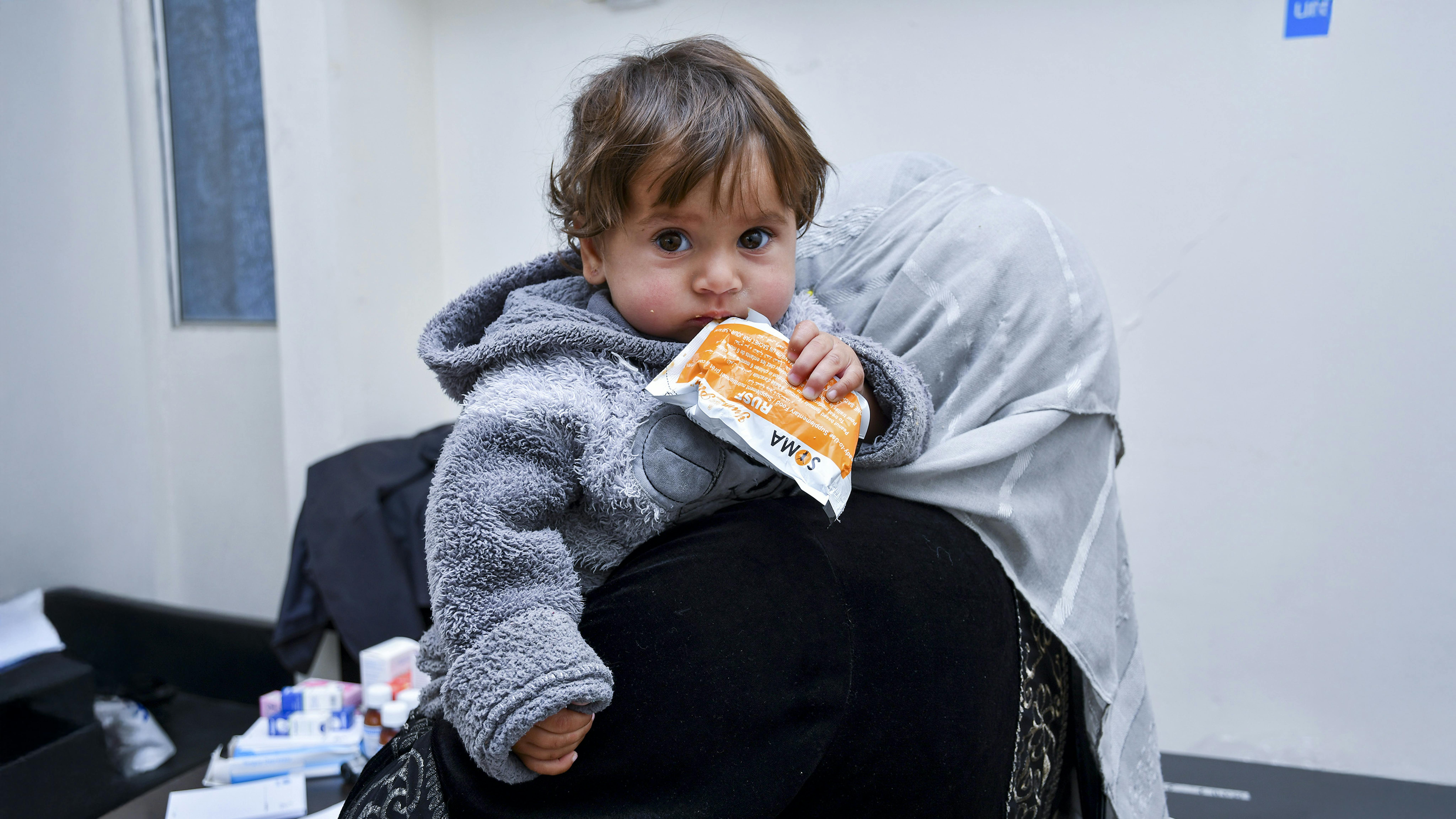 Siria - Raghad, una bambina di dieci mesi, tiene in mano del cibo terapeutico mentre sua madre riceve assistenza da un'équipe mobile supportata dall'UNICEF nella zona rurale di Damasco,