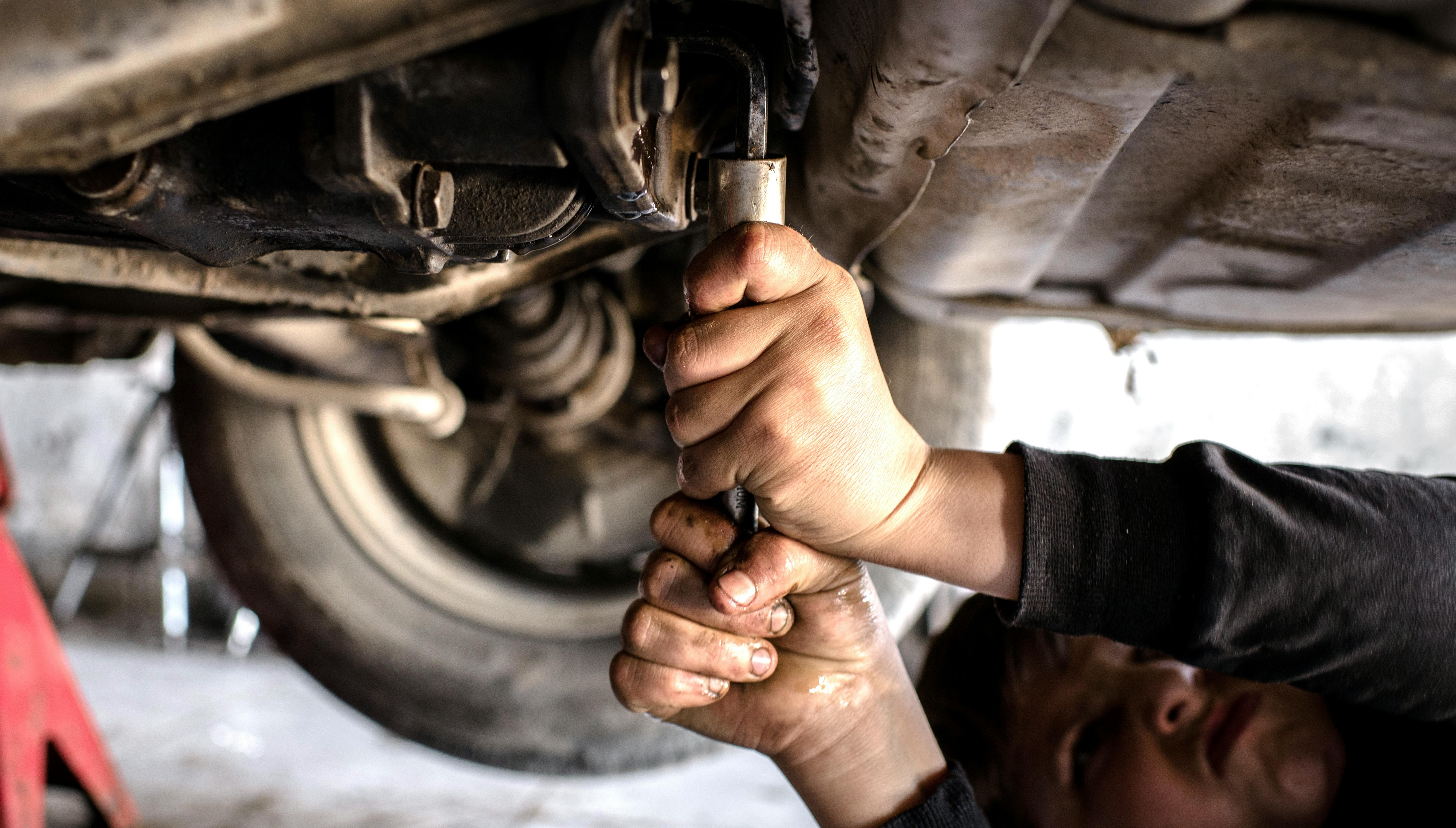 Un bambino a lavoro sotto una macchina, stringe con forza alcune componenti. Si tratta di un minorenne che lavora