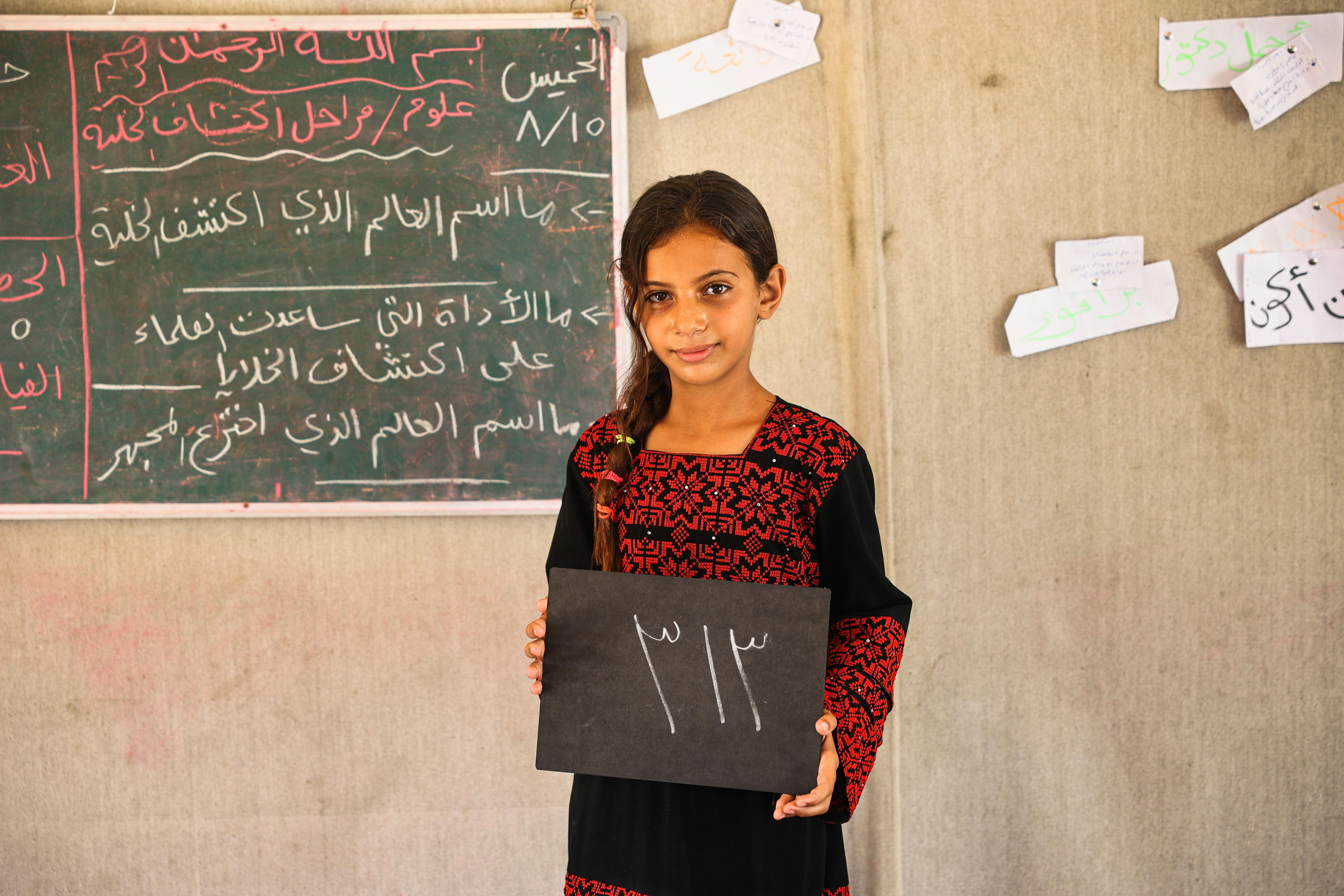 Agosto 2024, nel campo di Deir Al-Balah nella Striscia di Gaza, nello Stato di Palestina, Nevan, 11 anni, tiene in mano una lavagna su cui è scritto il numero di giorni di scuola persi: 313.
