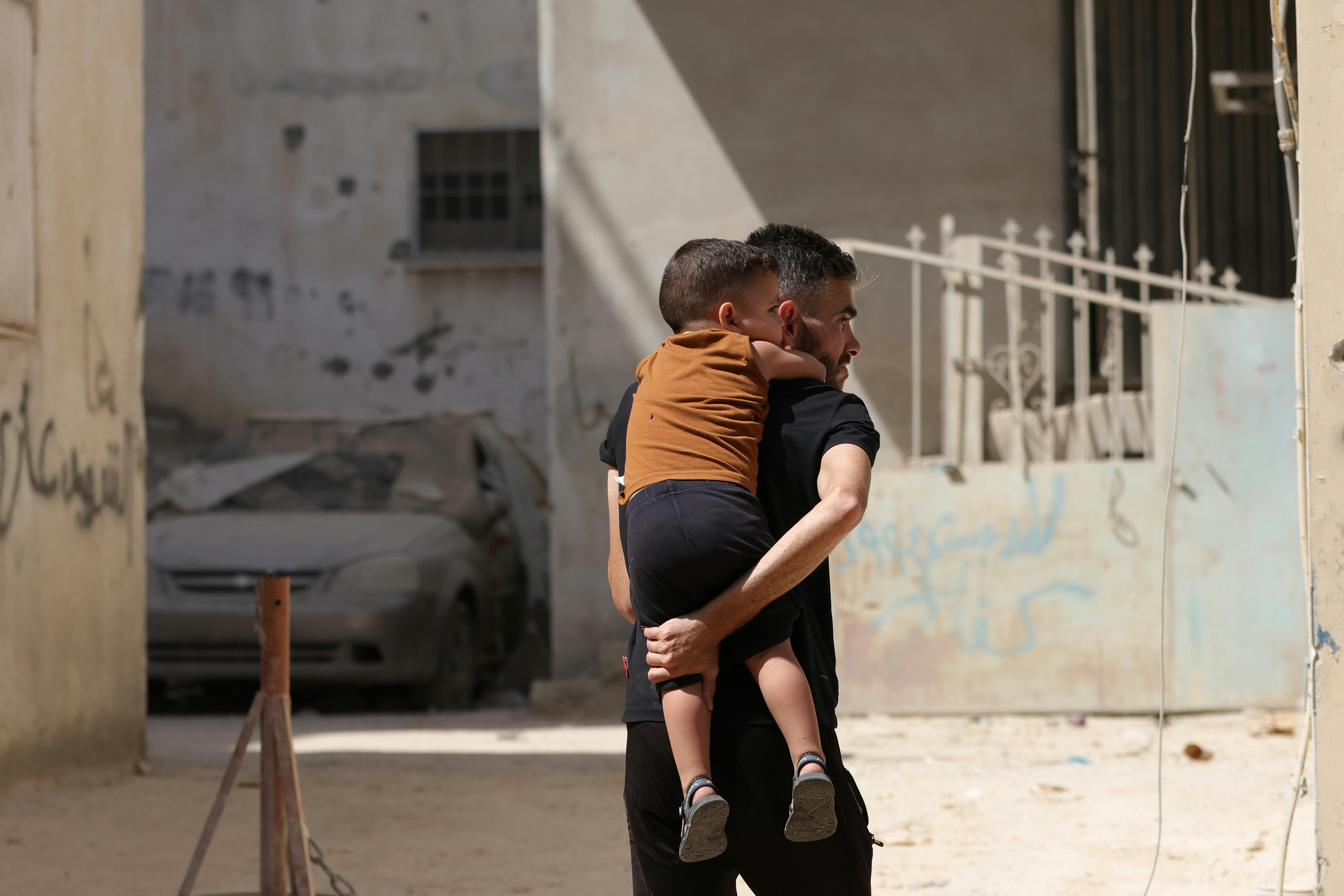 Un padre porta il figlio piccolo sulle spalle, mentre si muove nella città distrutta. Siamo nella Striscia di Gaza