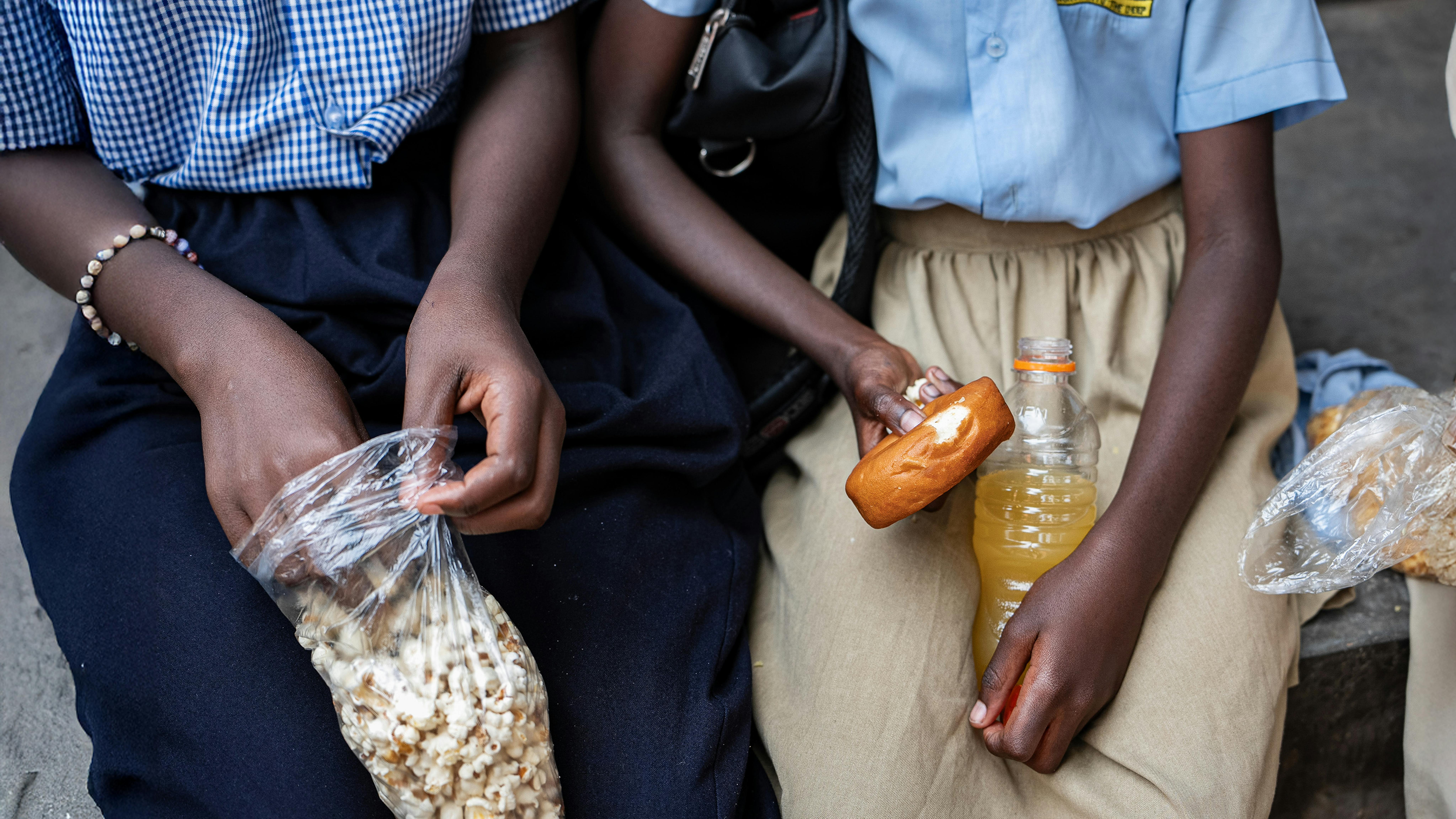 Kampala, Uganda, due bambini mangiano popcorn e pasticcini e bevono bevande zuccherate durante una pausa tra le lezioni nella loro scuola.