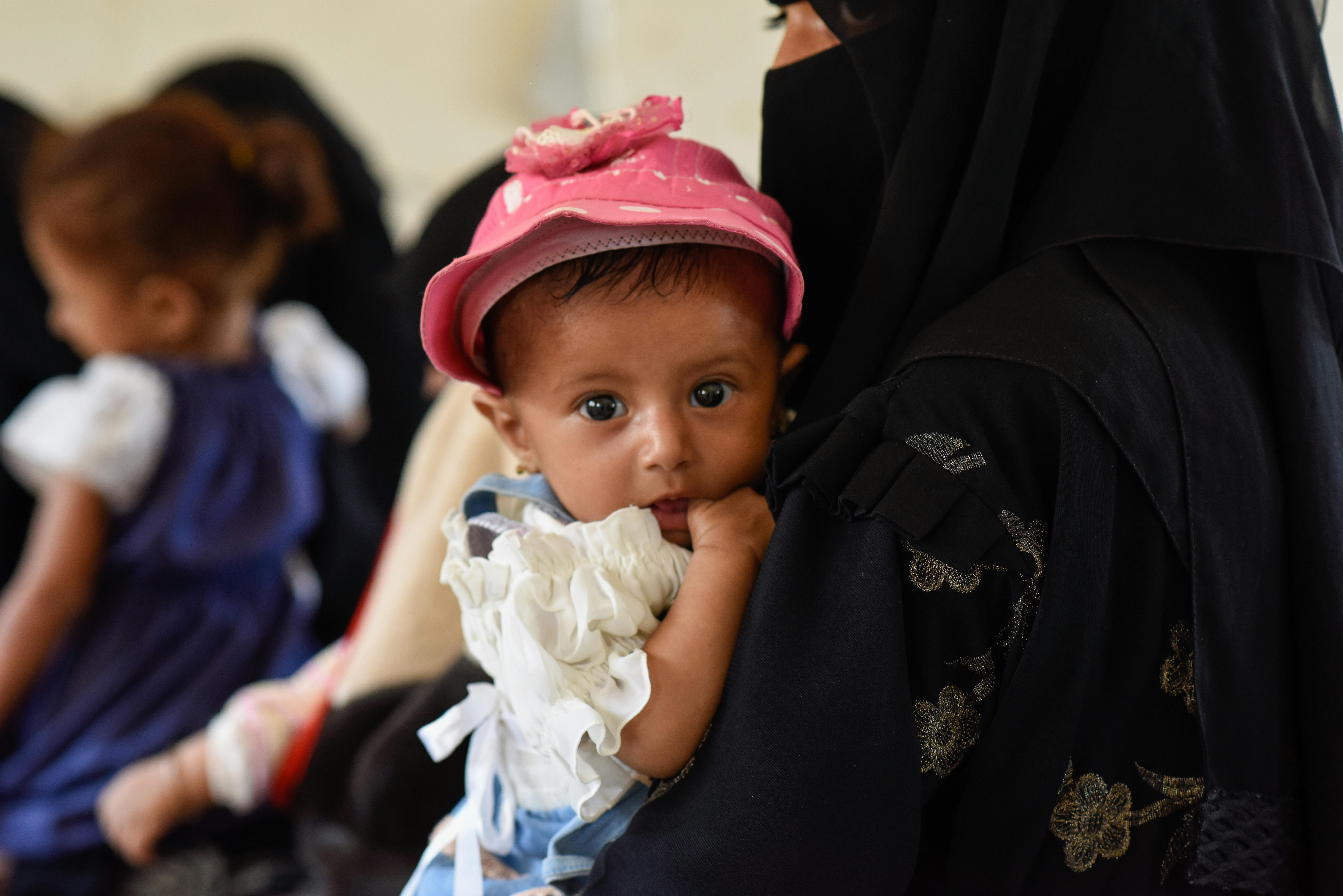 Revan, una bambina di 6 mesi, è cullata tra le braccia della madre mentre si sottopone agli screening e alle vaccinazioni obbligatorie, all'interno della clinica mobile, in Yemen