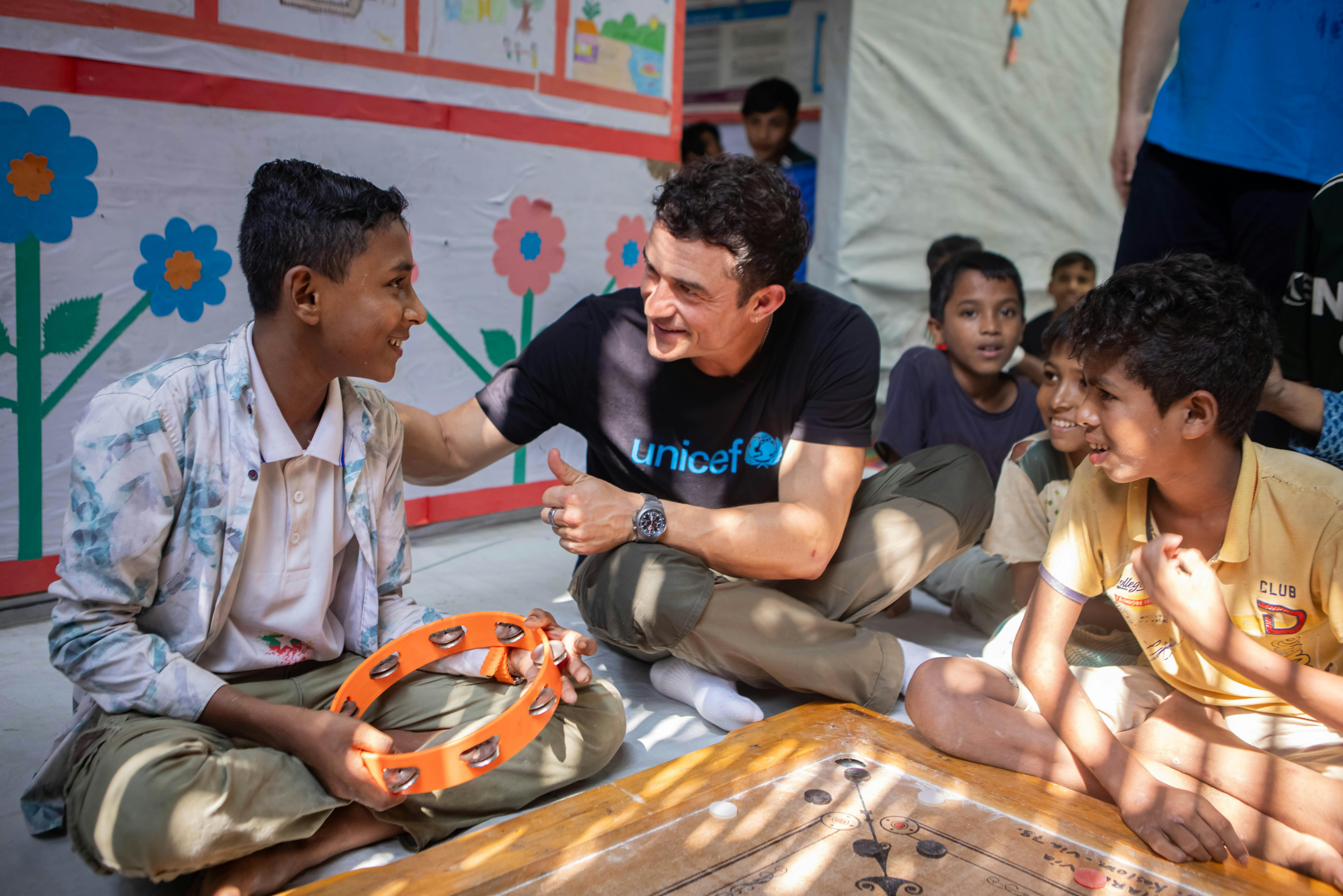 Il 6 novembre 2025, in Bangladesh, l'Ambasciatore di Buona Volontà dell'UNICEF Orlando Bloom parla con Kaiser, 15 anni, durante la visita al Centro Polivalente per bambini e adolescenti del Campo 4, a Cox's Bazar. Il notevole talento canoro di Kawser e la sua crescente piattaforma YouTube riflettono le aspirazioni e la resilienza dei giovani Rohingya. Come molti adolescenti del centro, Kawser sta accedendo a un supporto strutturato per coltivare il suo talento e costruire un futuro di speranza.